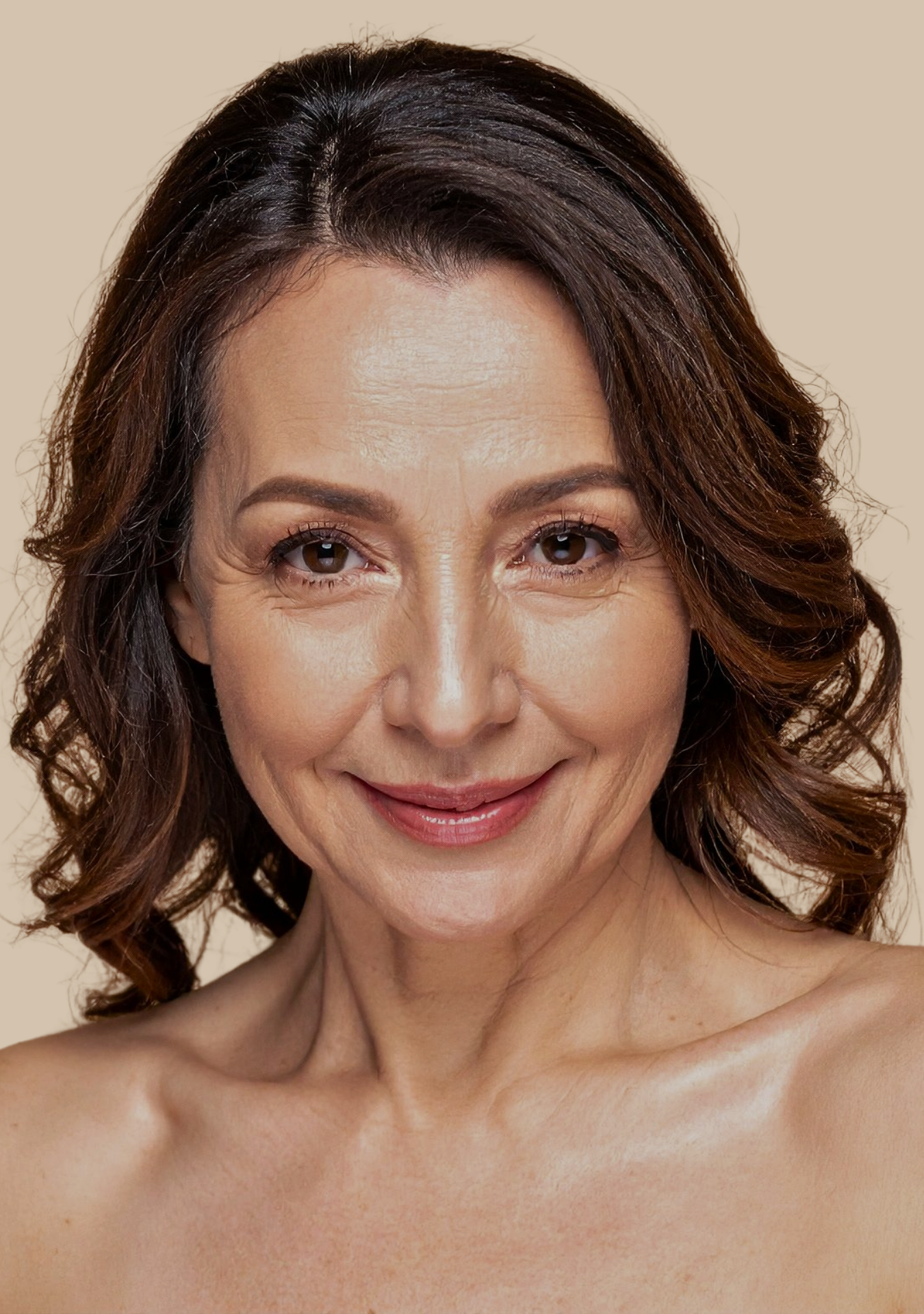 Retrato de una mujer de cabello castaño con rizos, sonriendo, con piel clara, sin ropa visible en la parte superior, fondo beige. Muy bien iluminada, expresión alegre y natural.