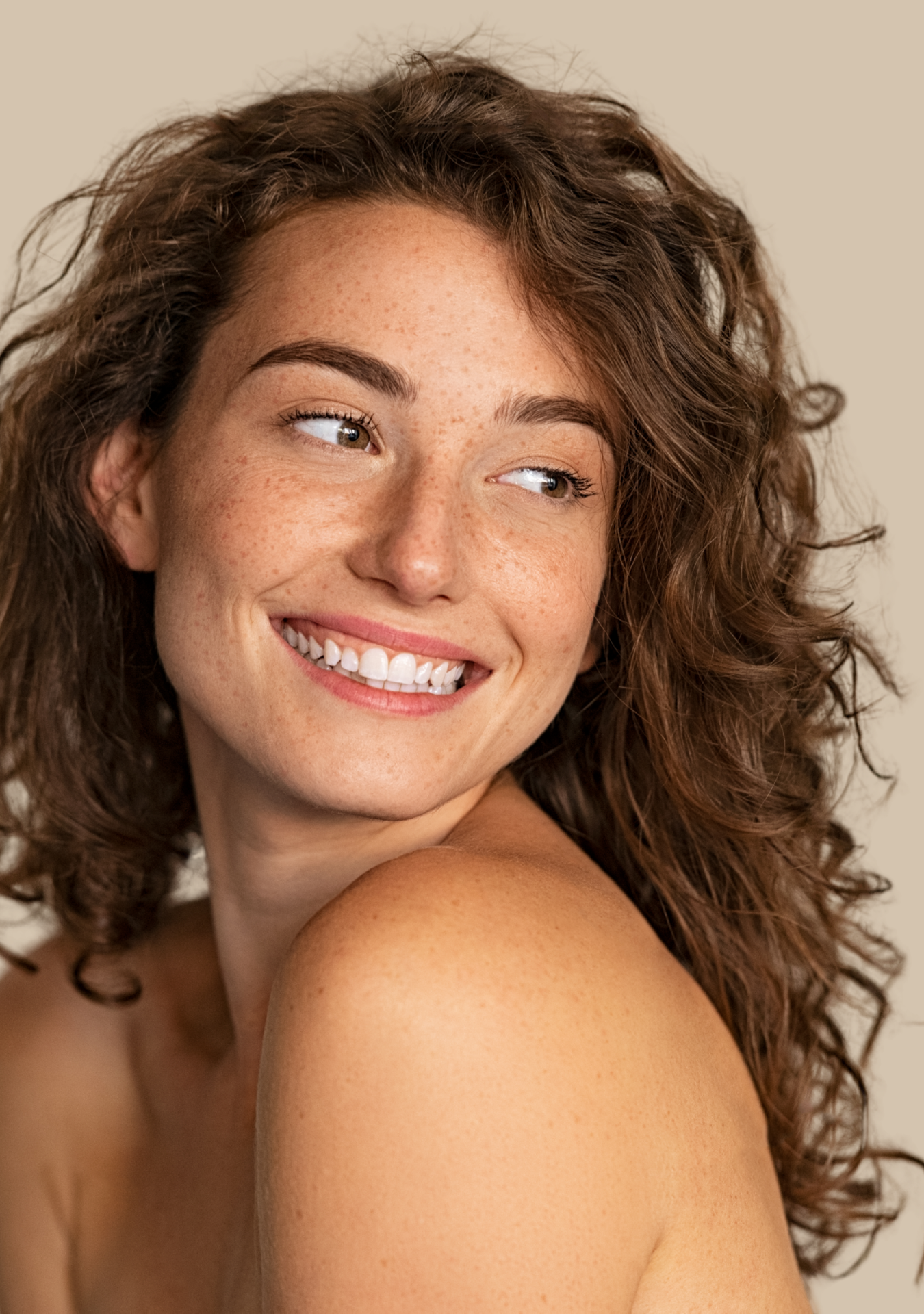 Joven mujer con cabello rizado y rubio, sonriendo y mirando hacia la izquierda, con piel clara y pecas.