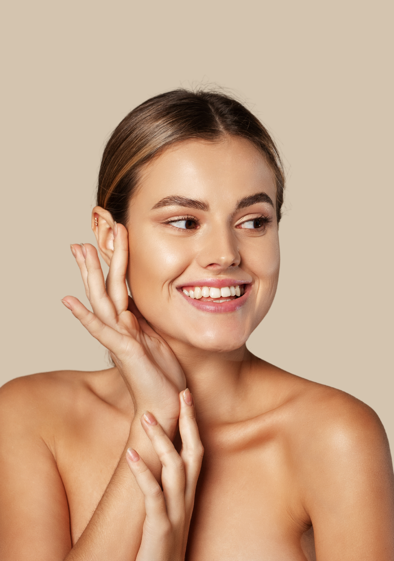 Mujer joven sonriendo, tocándose la cara y el cuello, con piel clara y cabello castaño, fondo beige.