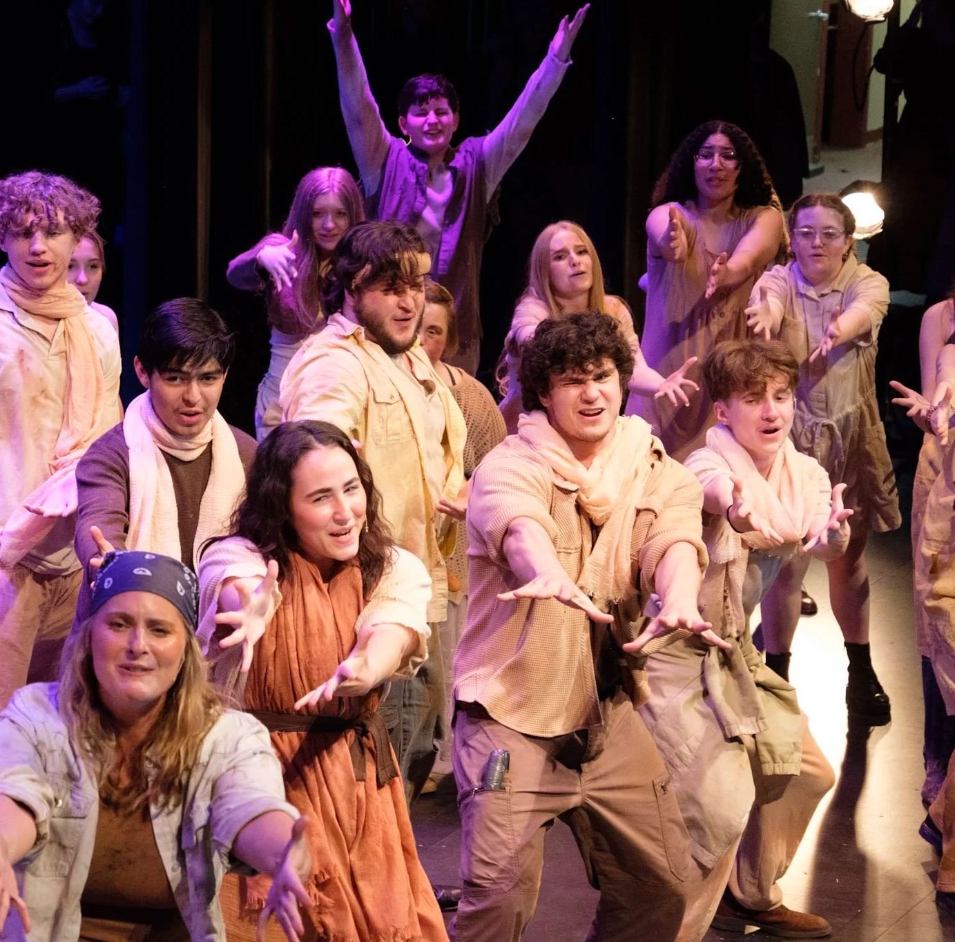 Group of performers on stage in theatrical costumes, engaged in a lively performance with expressive poses and facial expressions.