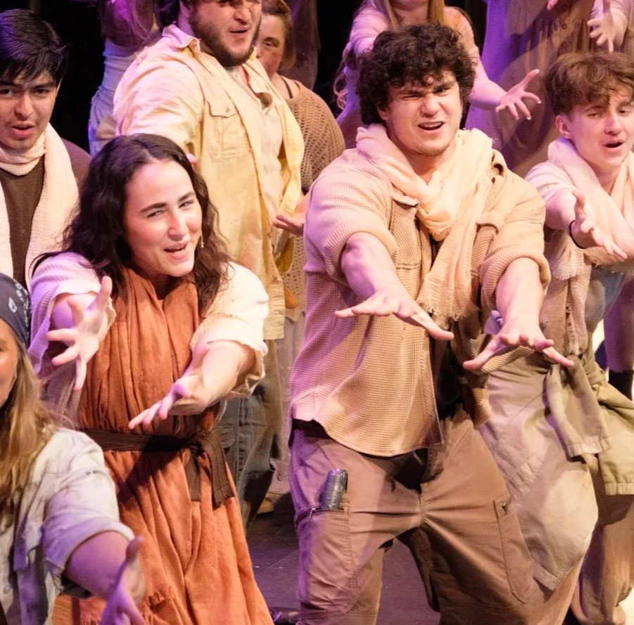 Group of performers on stage in theatrical costumes, engaged in a lively performance with expressive poses and facial expressions.