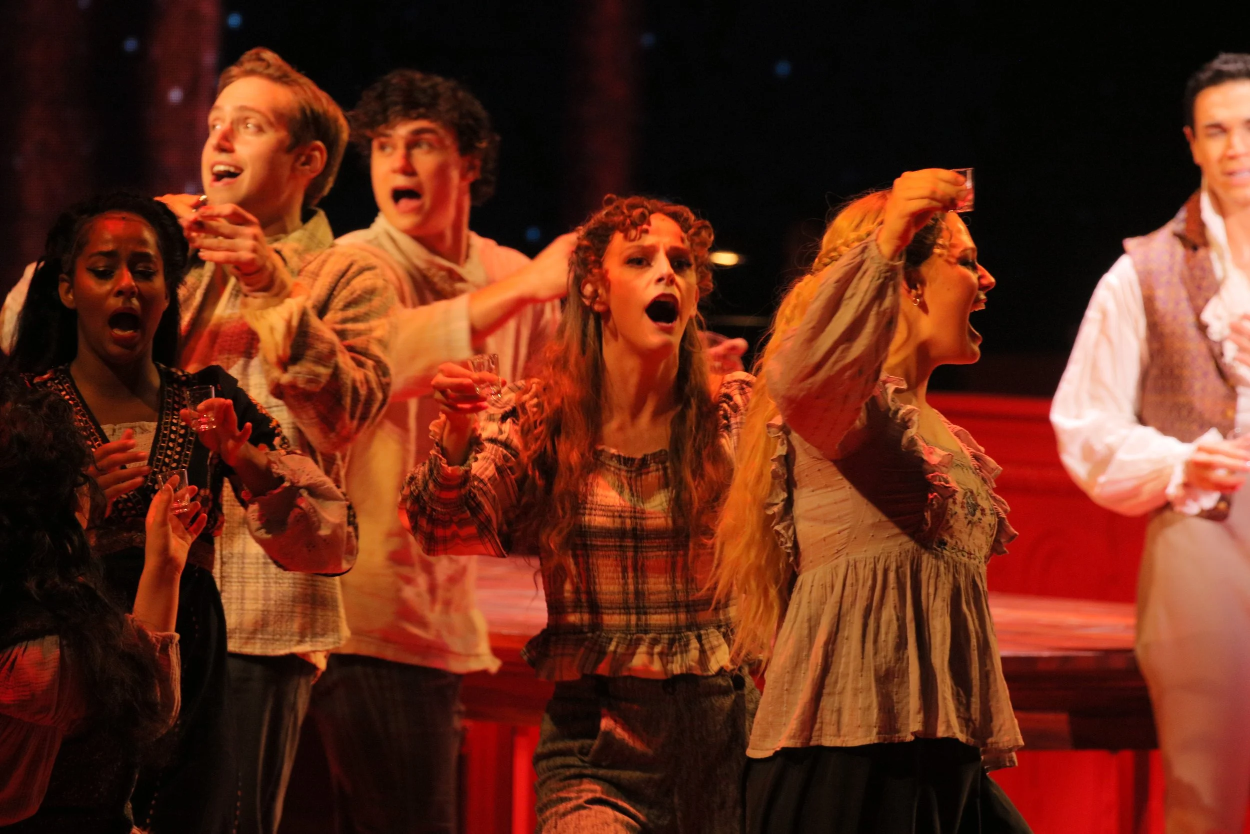 Cast members performing on stage, dressed in period costumes, expressing intense emotion in a theatrical production.