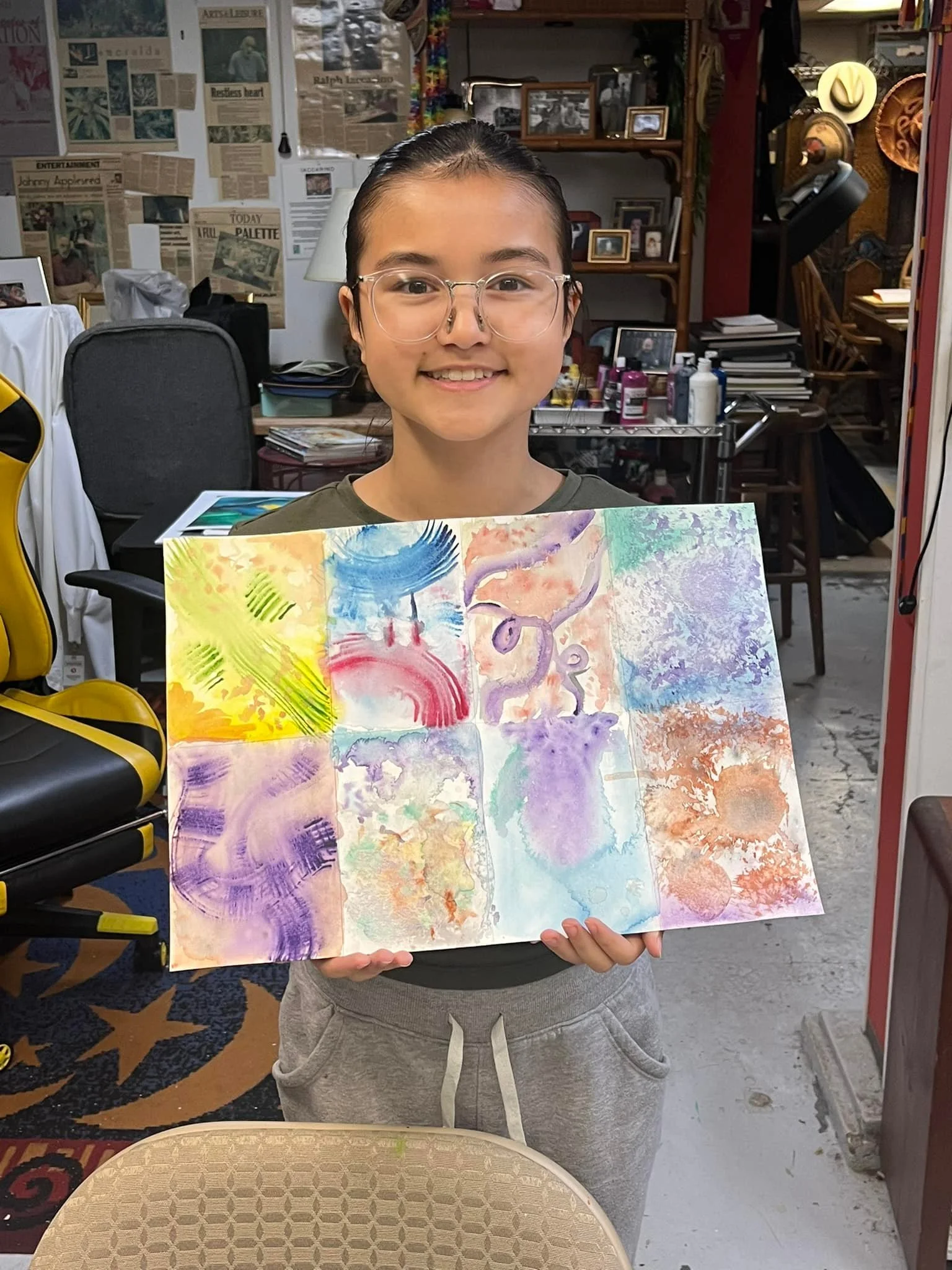 A student of Raphael Iaccarino's holding a colorful abstract watercolor painting in a cluttered art studio or classroom.