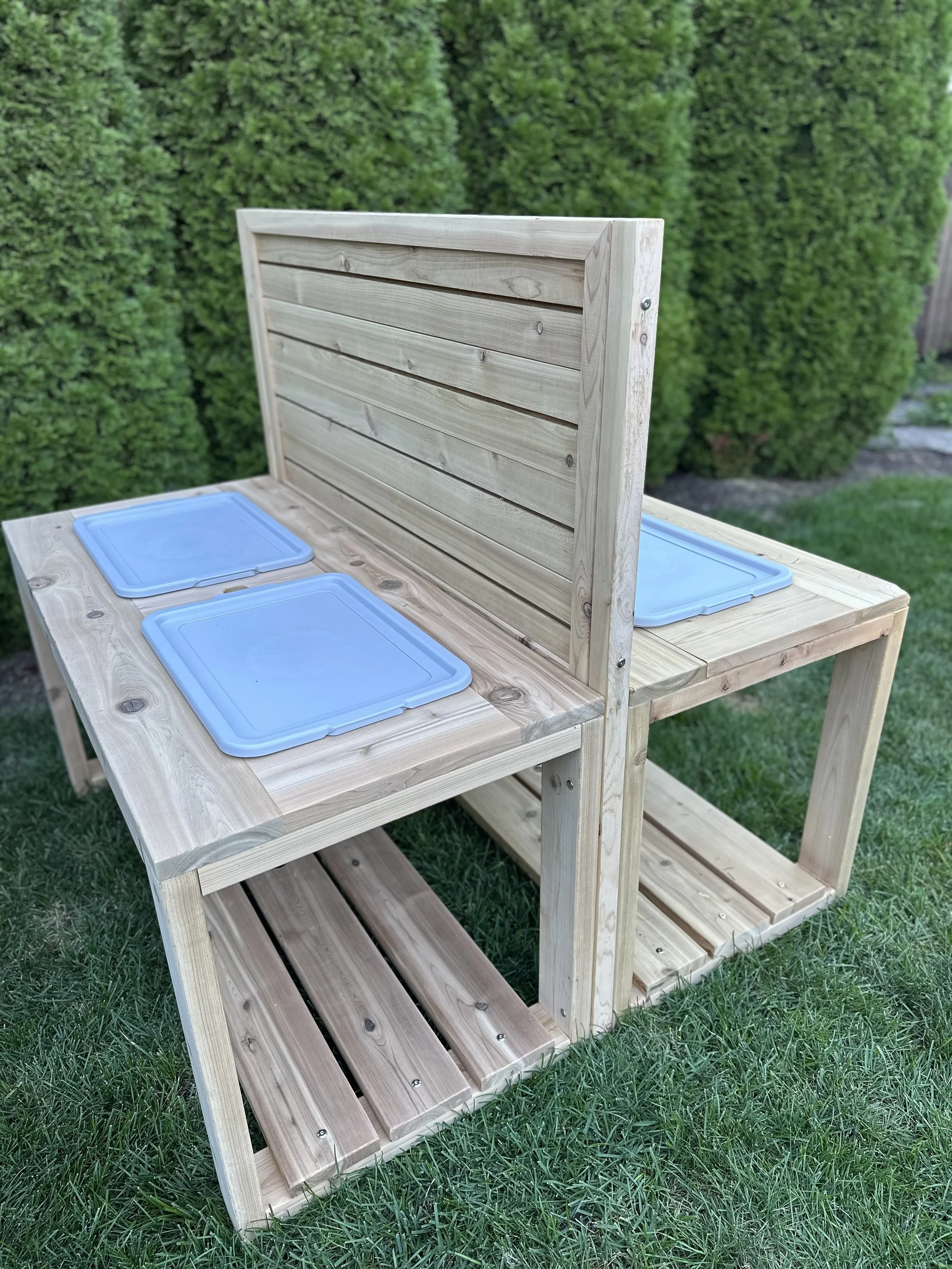 A handcrafted double-sided Red Cedar sensory station featuring a sturdy dual-table design and a central vertical activity slat wall.