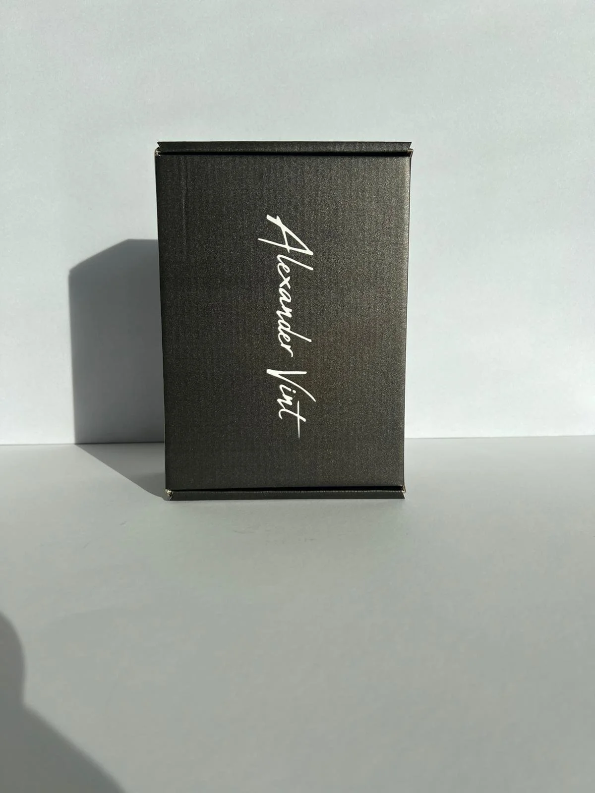 Schwarze Verpackung mit weißen, handgeschriebenen Schriftzug "Heidnischer Völk" auf weißem Hintergrund, Schatten links.