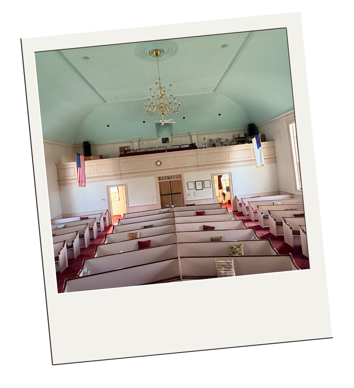 Inside a church with rows of pews, an American flag and a state flag hang from the balcony, which features a chandelier hanging from a high, light green ceiling.