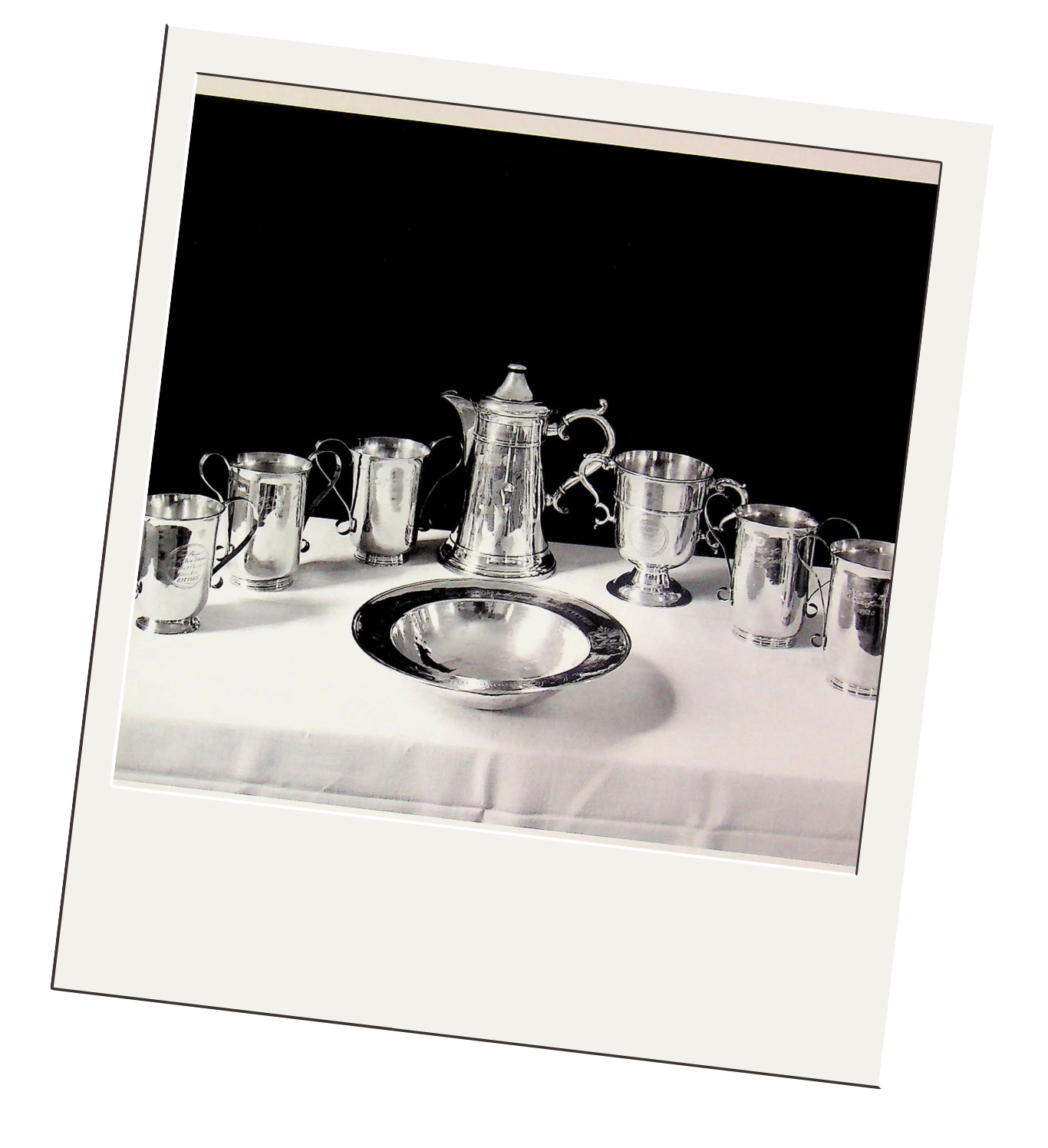 A collection of shiny silver tea set items, including a teapot, six cups with handles, a pitcher, and a tray, all arranged on a white tablecloth with a black background.