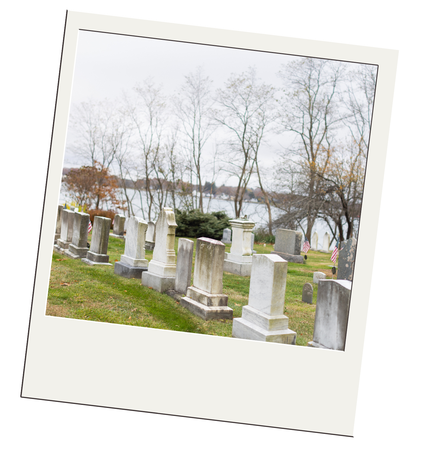 Graveyard with tombstones, trees, and a body of water in the background.