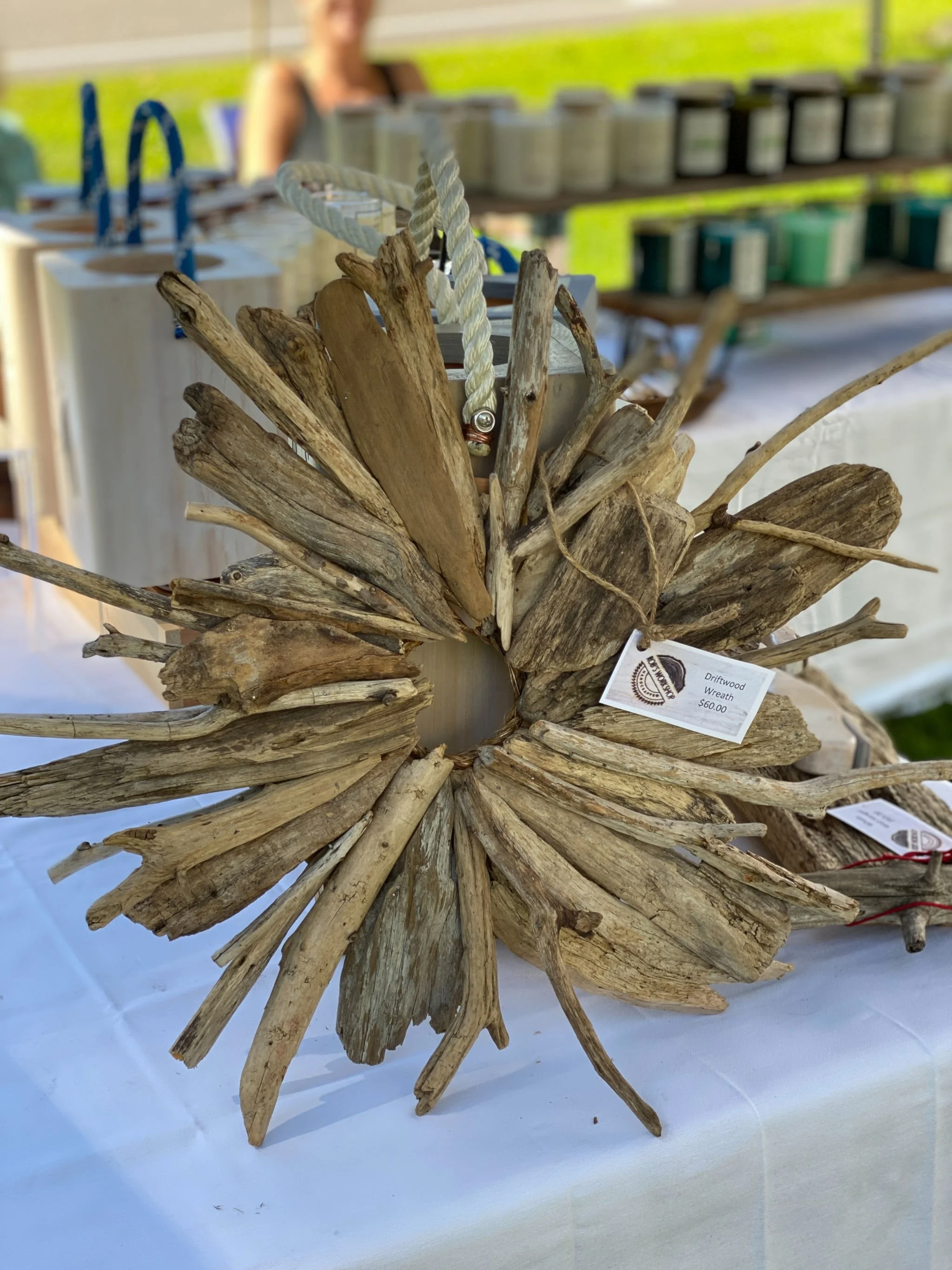 A driftwood wreath made of various pieces of weathered wood arranged in a circular pattern, with a tag indicating it costs $60.00.