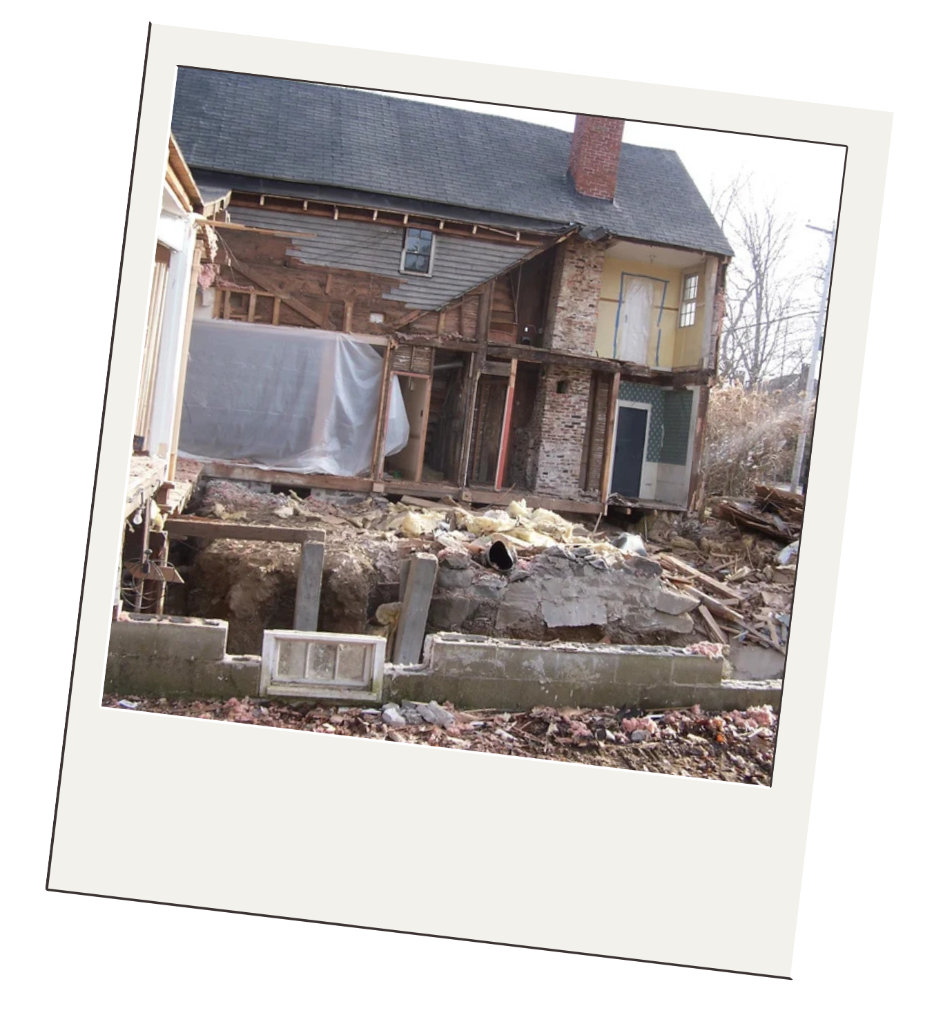 A house undergoing construction or renovation, with visible exposed framing, brickwork, and construction debris in the yard.