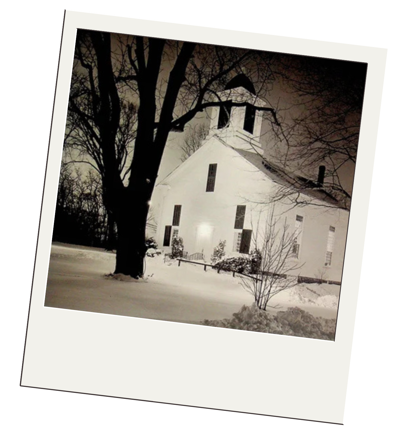 A nighttime snowy scene of a white church with a tall steeple and large windows, partially obscured by a large tree in the foreground.