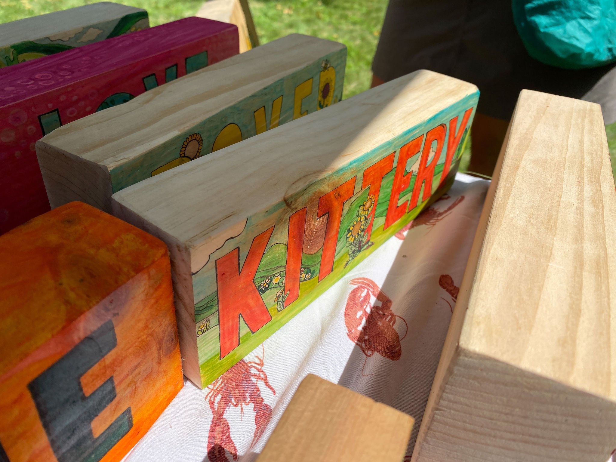Colorful painted wooden blocks on a table, with one block partially visible showing the word "LOVE" and decorated with flowers and sun illustrations.