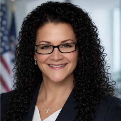 Portrait of a woman with curly dark hair wearing a turquoise blazer, smiling at the camera.