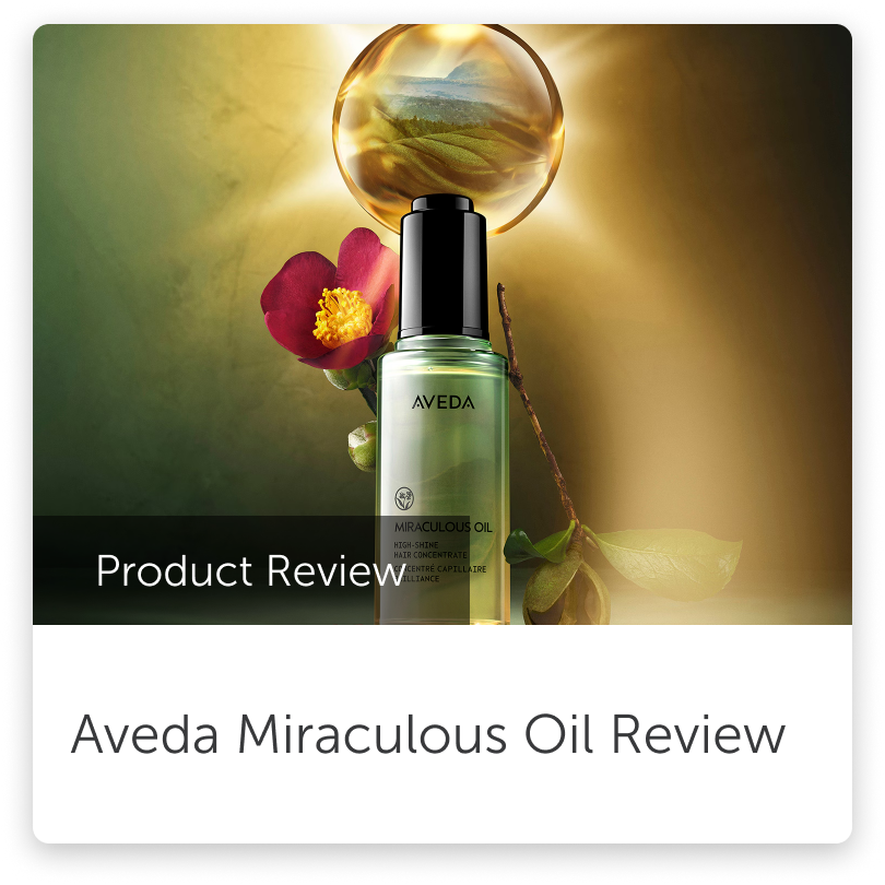 A bottle of Aveda Miraculous Oil hair treatment with a red flower and green leaves, a reflective glass sphere showing a landscape scene, and a gradient background in green and gold tones.