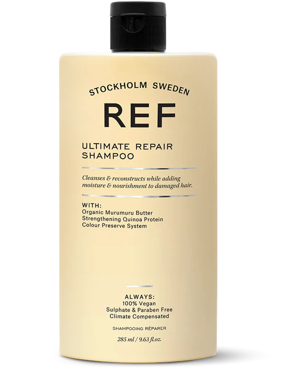 A beige bottle of REF Ultimate Repair Shampoo with black flip cap, featuring black text and metallic accents, against a black background.
