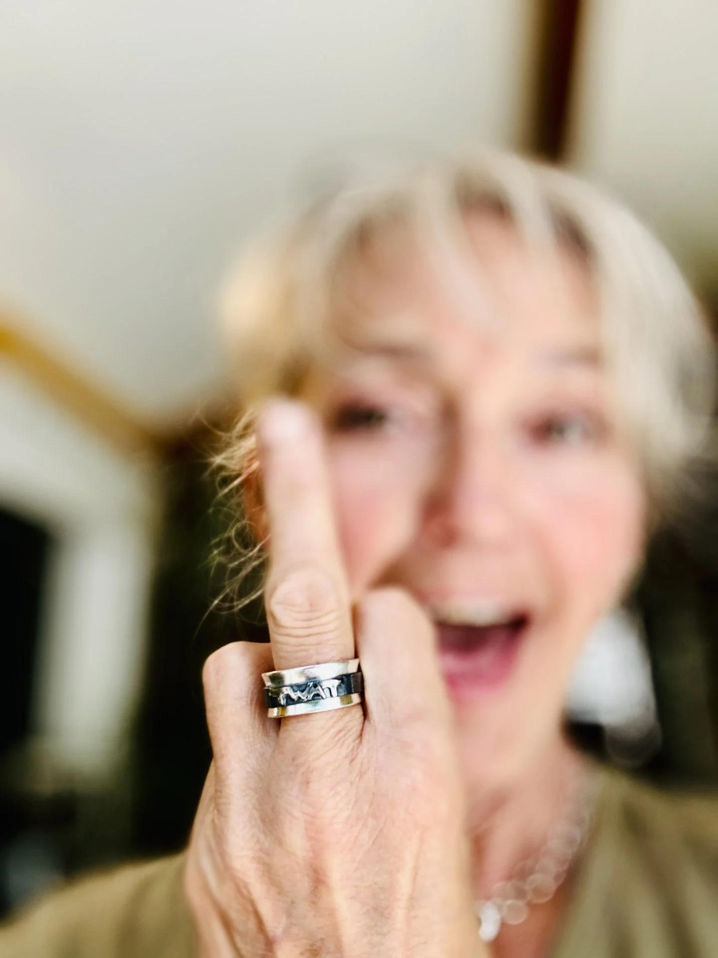 A woman with short blond hair smiling and showing her middle finger, which has a silver ring with the word twat on it.