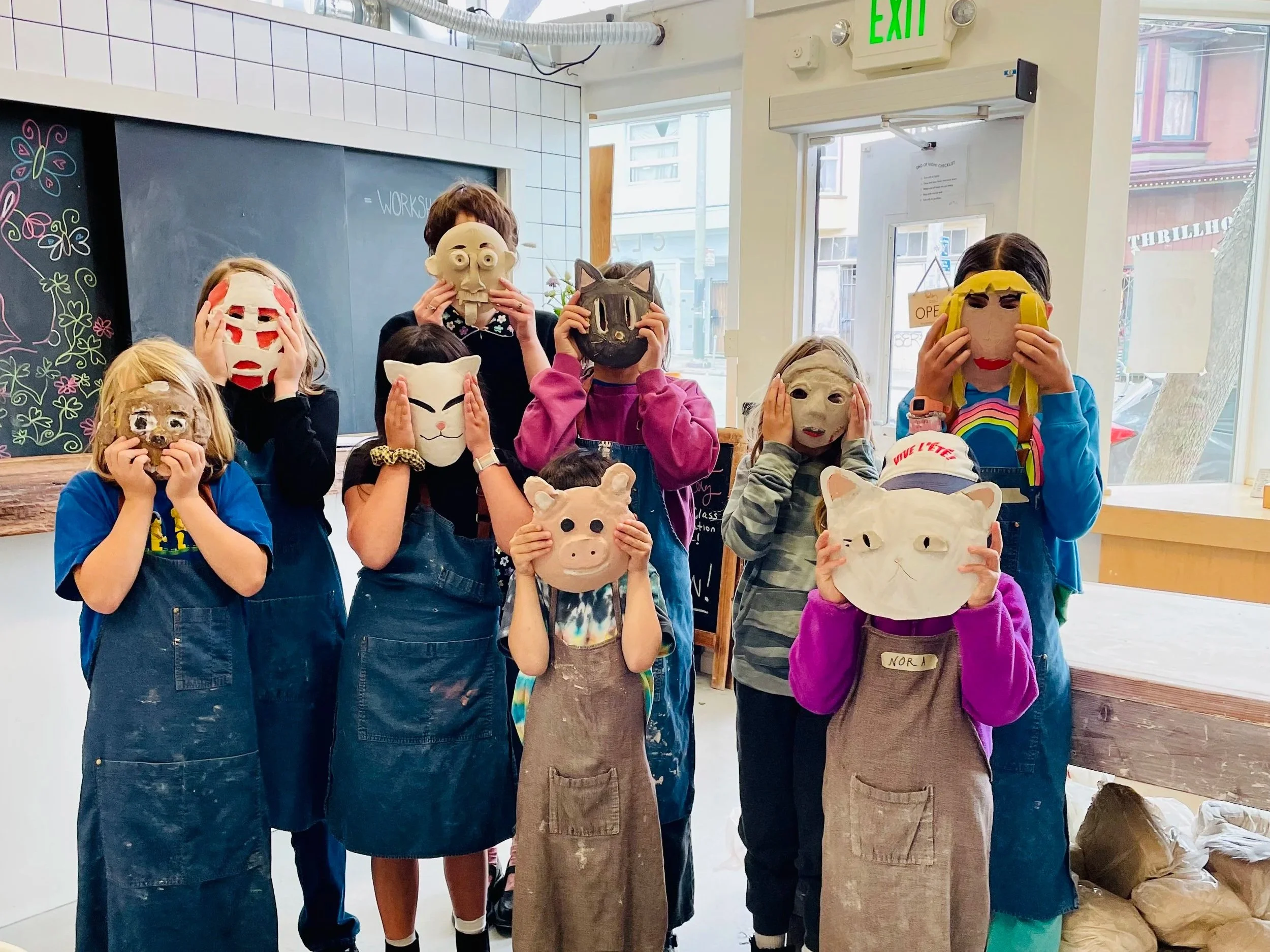 A group of kids hold up their summer camp masks made from clay