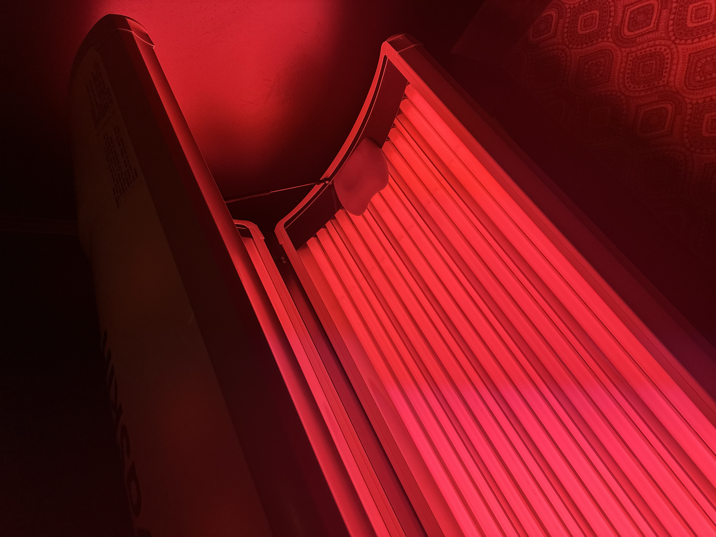 A red tanning bed with its door open, showing the lighted tanning surface inside.