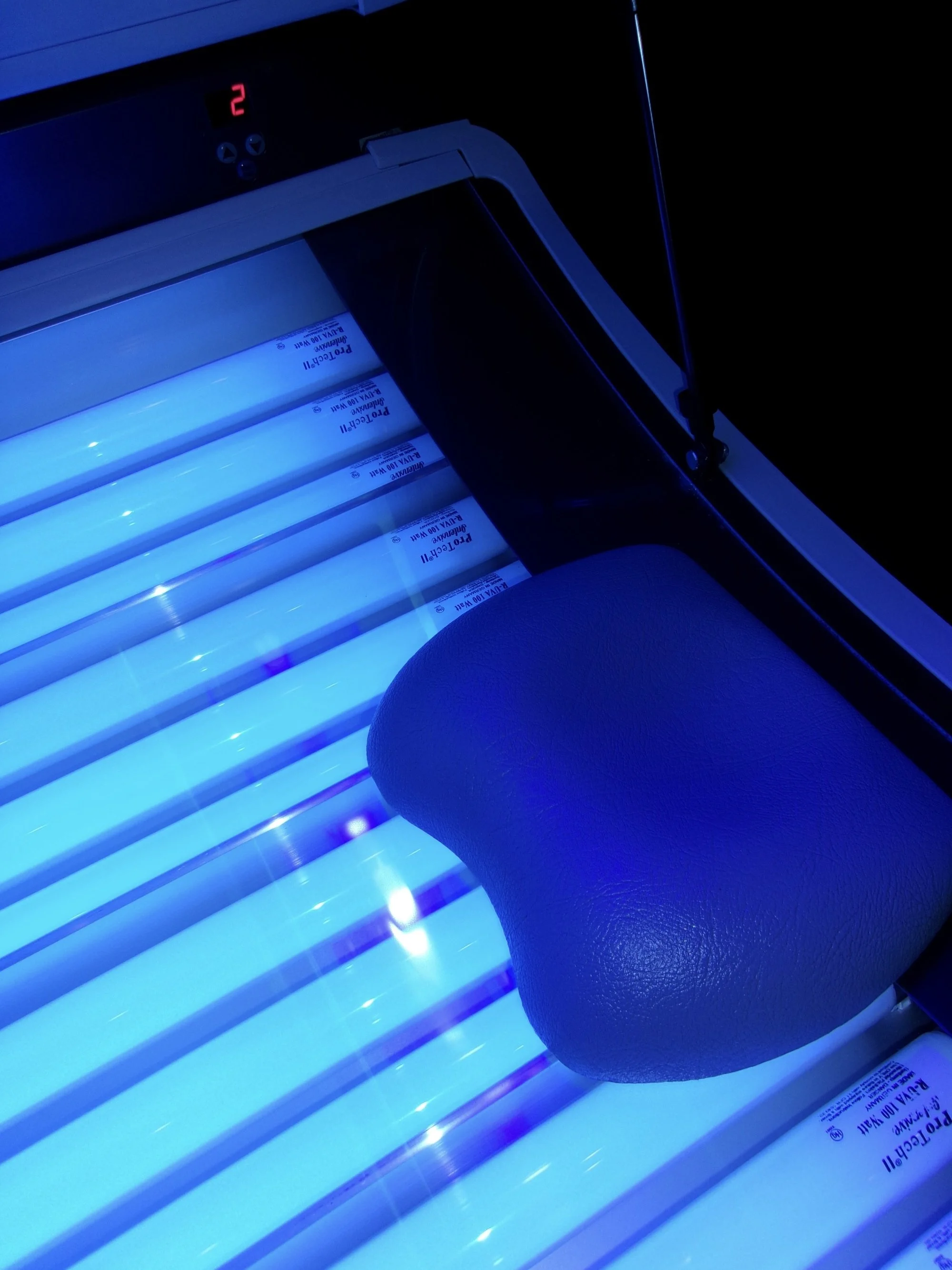 Indoor tanning bed with blue UV lights and a cushioned head rest.