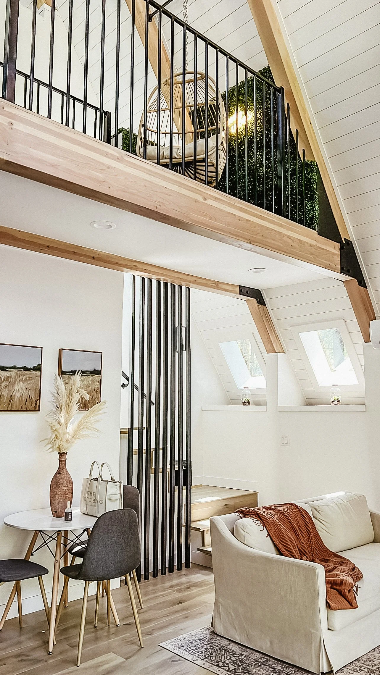 Interior view of a modern living space with a staircase, a seating area, and a loft with a hanging chair and greenery.