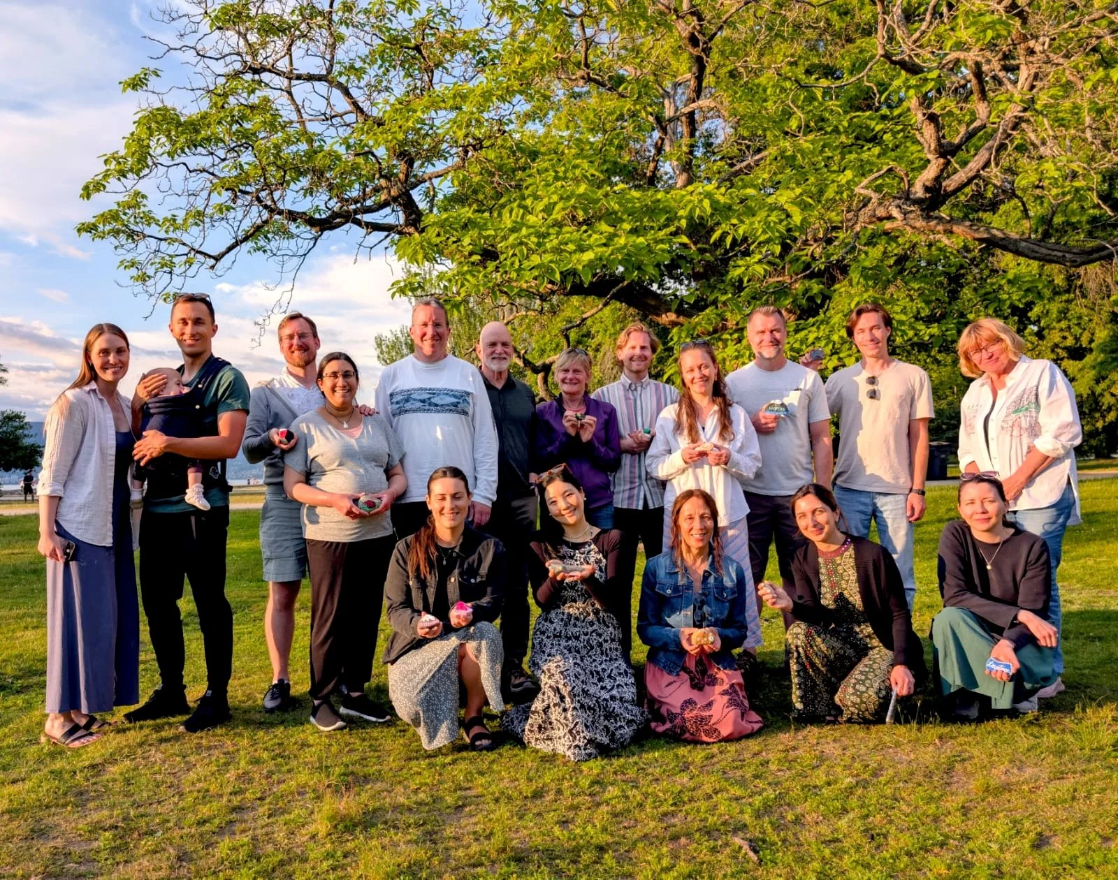 About twenty Art Cafe participants pose together on the grass under a large tree on a sunny evening