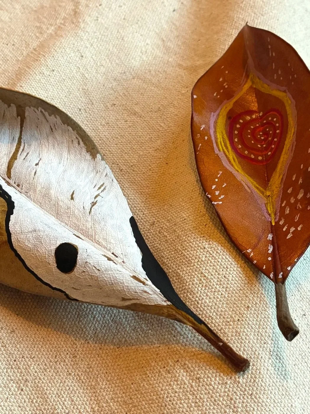 Two dried leaves painted with an eye and a seed design
