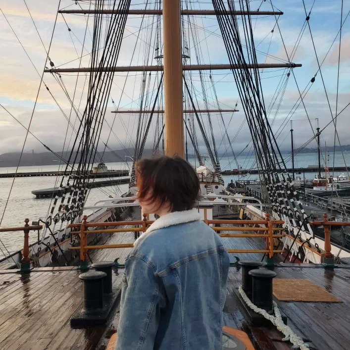 Young woman with short hair facing away from the camera with sail masts in front of her