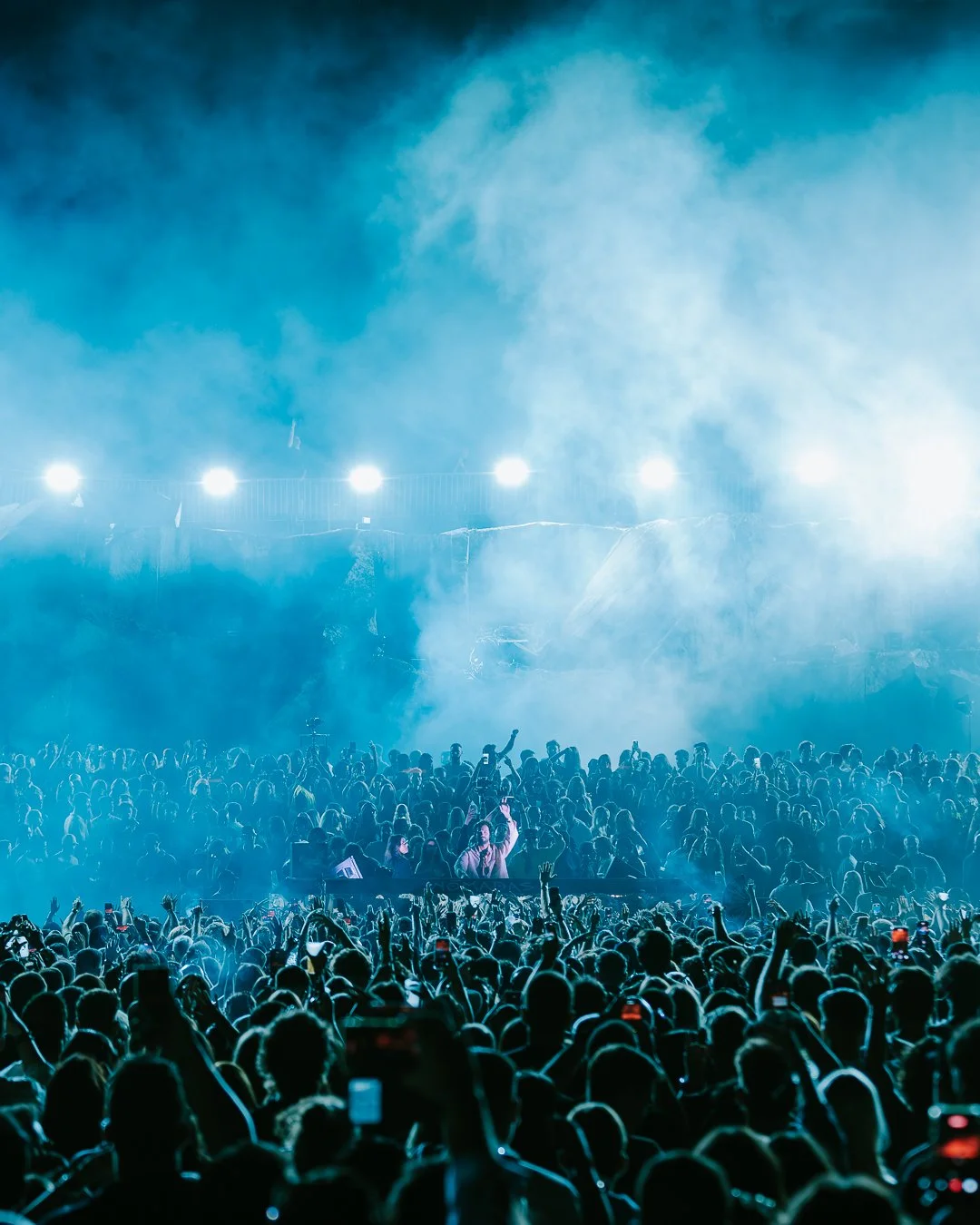 Crowd of people at a festival with blue lighting and smoke effects.