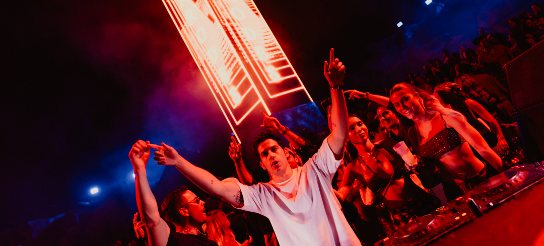 Arodes performs at a nightclub with a large crowd dancing, illuminated by vibrant red and blue lights.