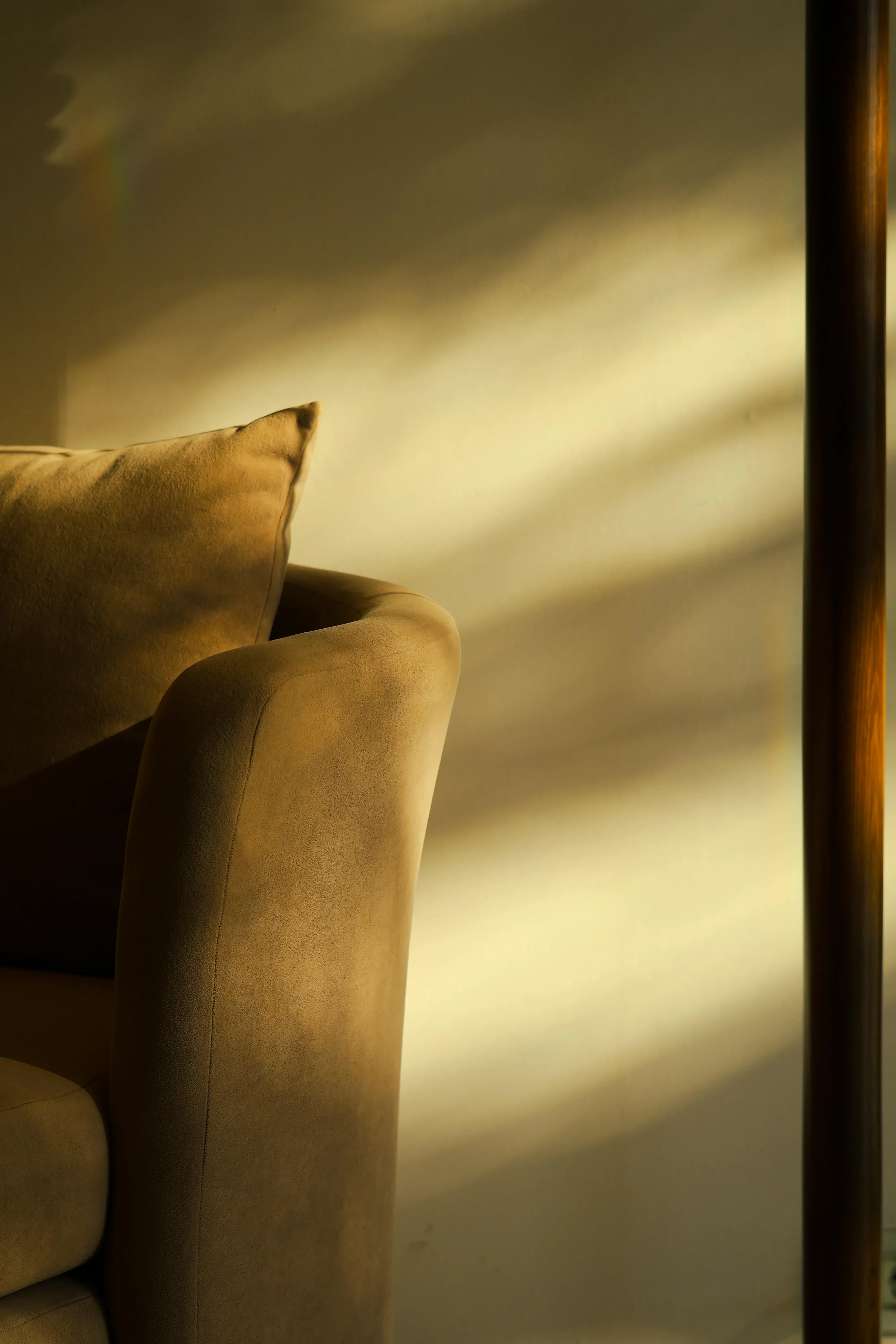 Close-up of a beige sofa with a pillow, illuminated by warm yellow lighting, next to a wooden lamp.