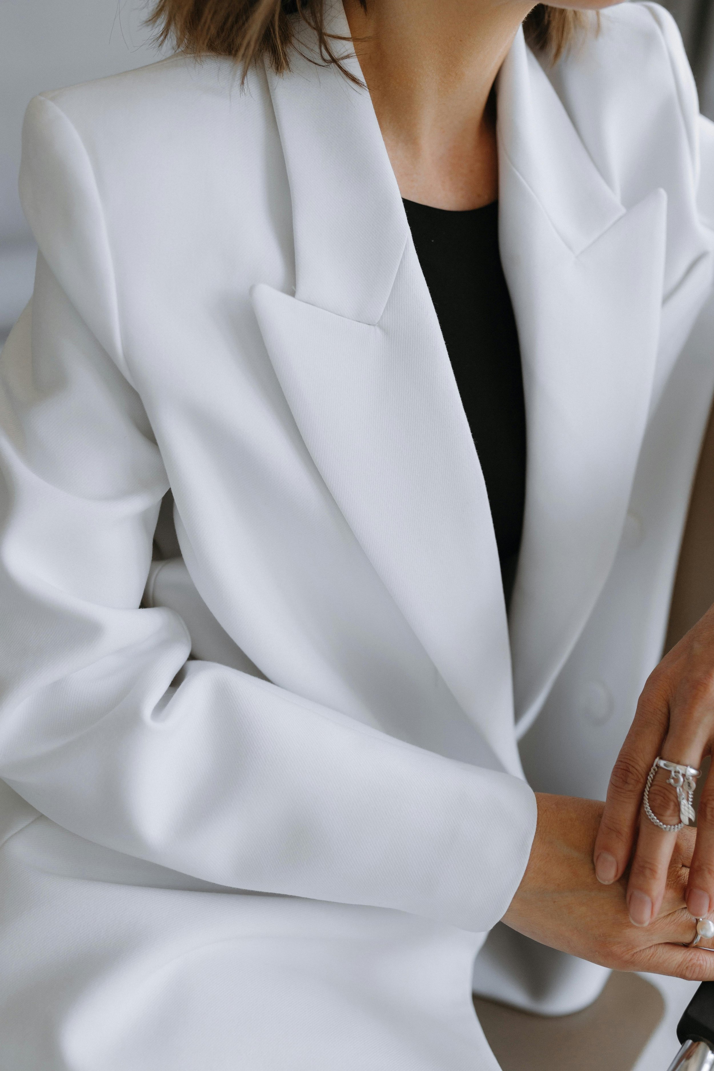 Close-up of a person wearing a white blazer over a black top, with jewelry on their hand.
