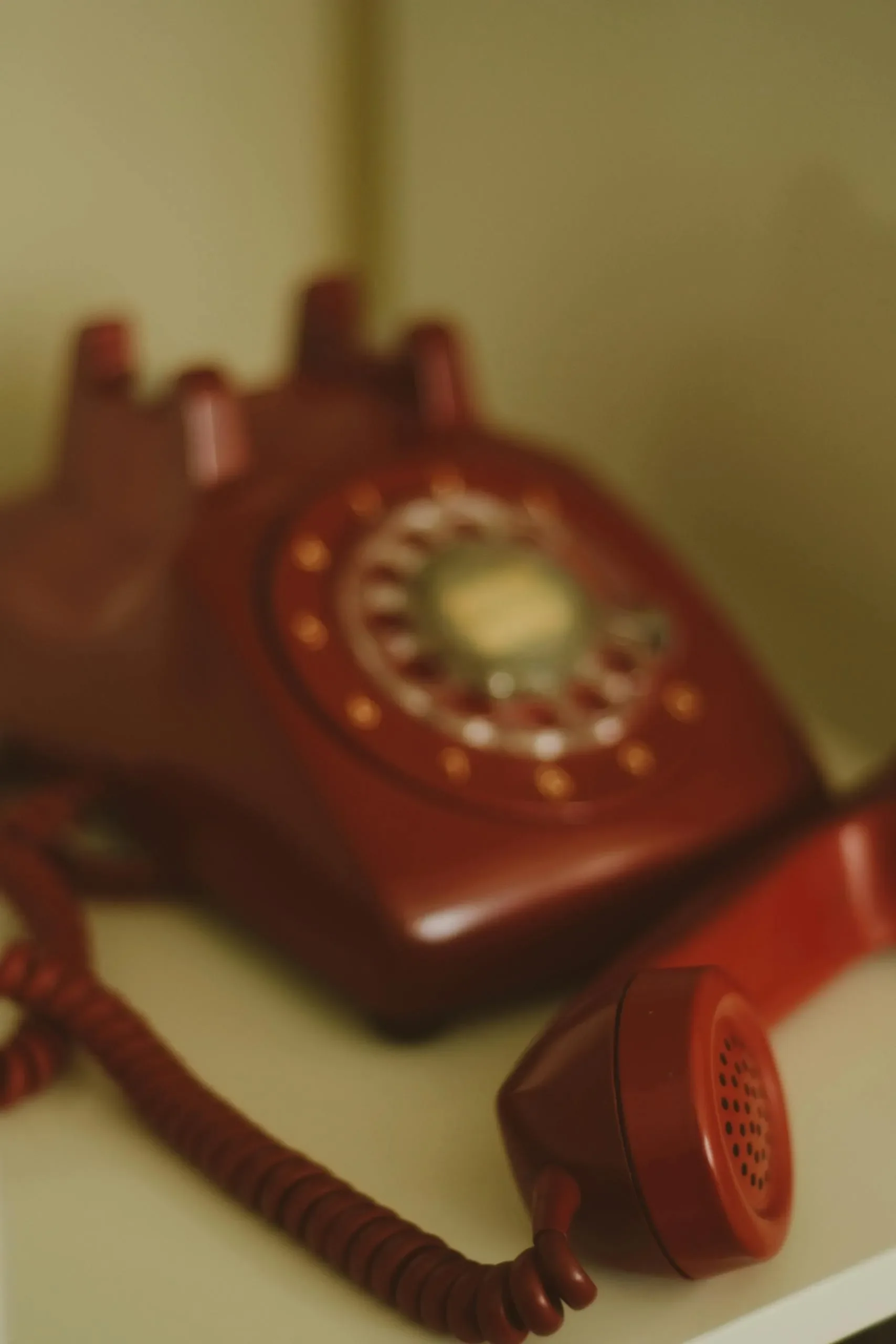 A vintage red rotary telephone placed on a light-colored surface with a muted background.