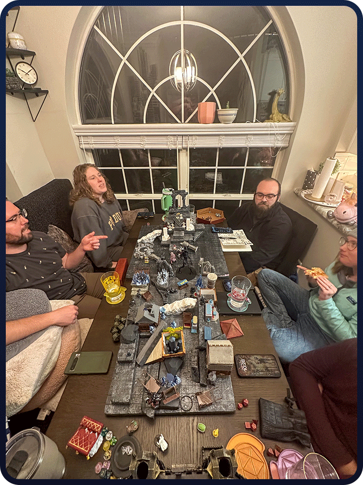 Group of five people sitting around a dining table playing a tabletop role-playing game with miniature figures and game accessories.