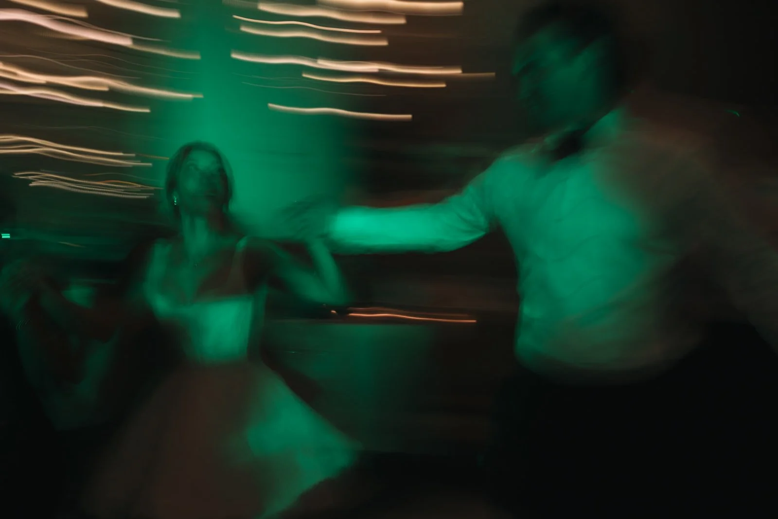 Blurry image of a man and woman dancing in a dimly lit setting with green lighting, with motion streaks in the background.