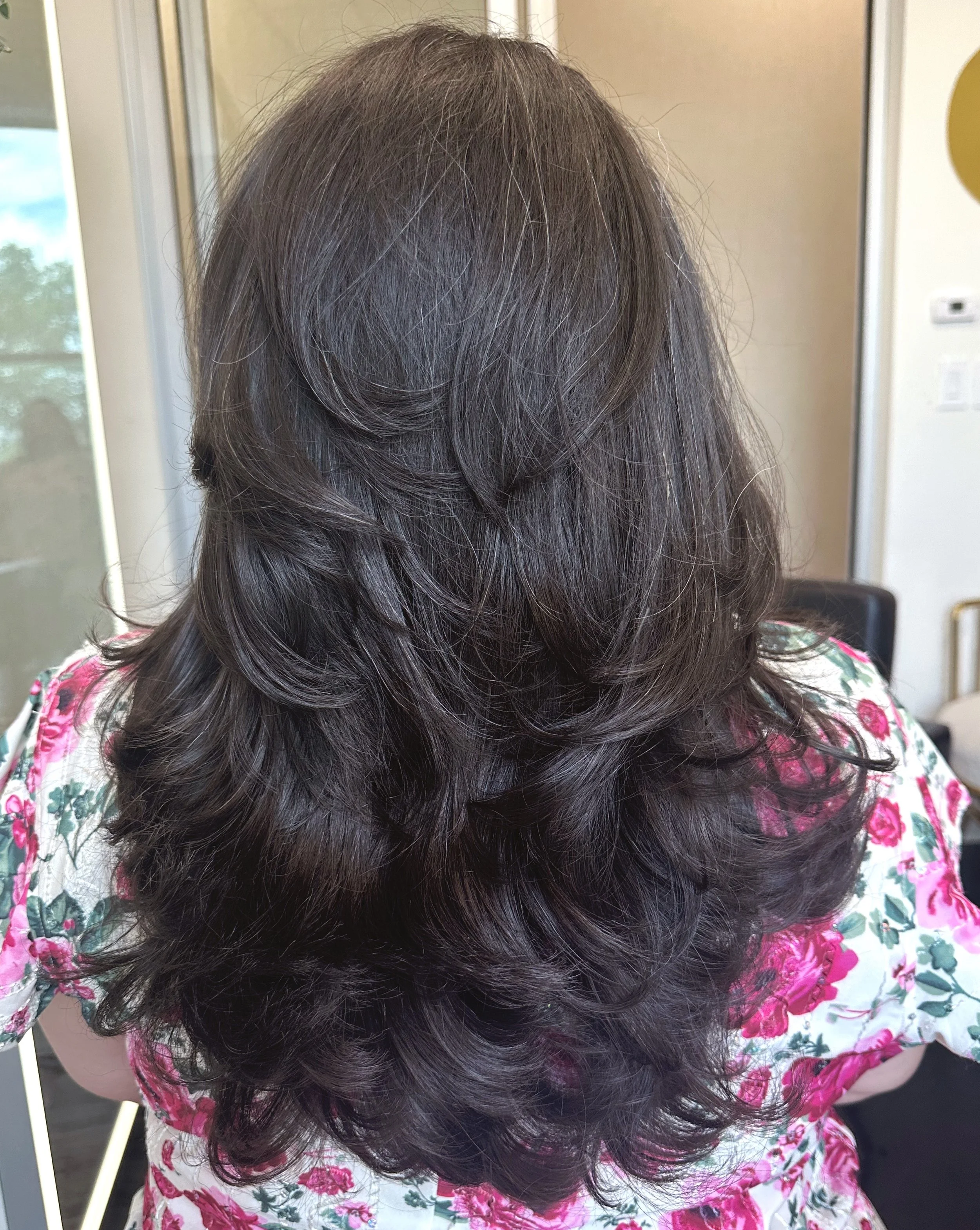 A photo of a client with long dark hair with soft waves.