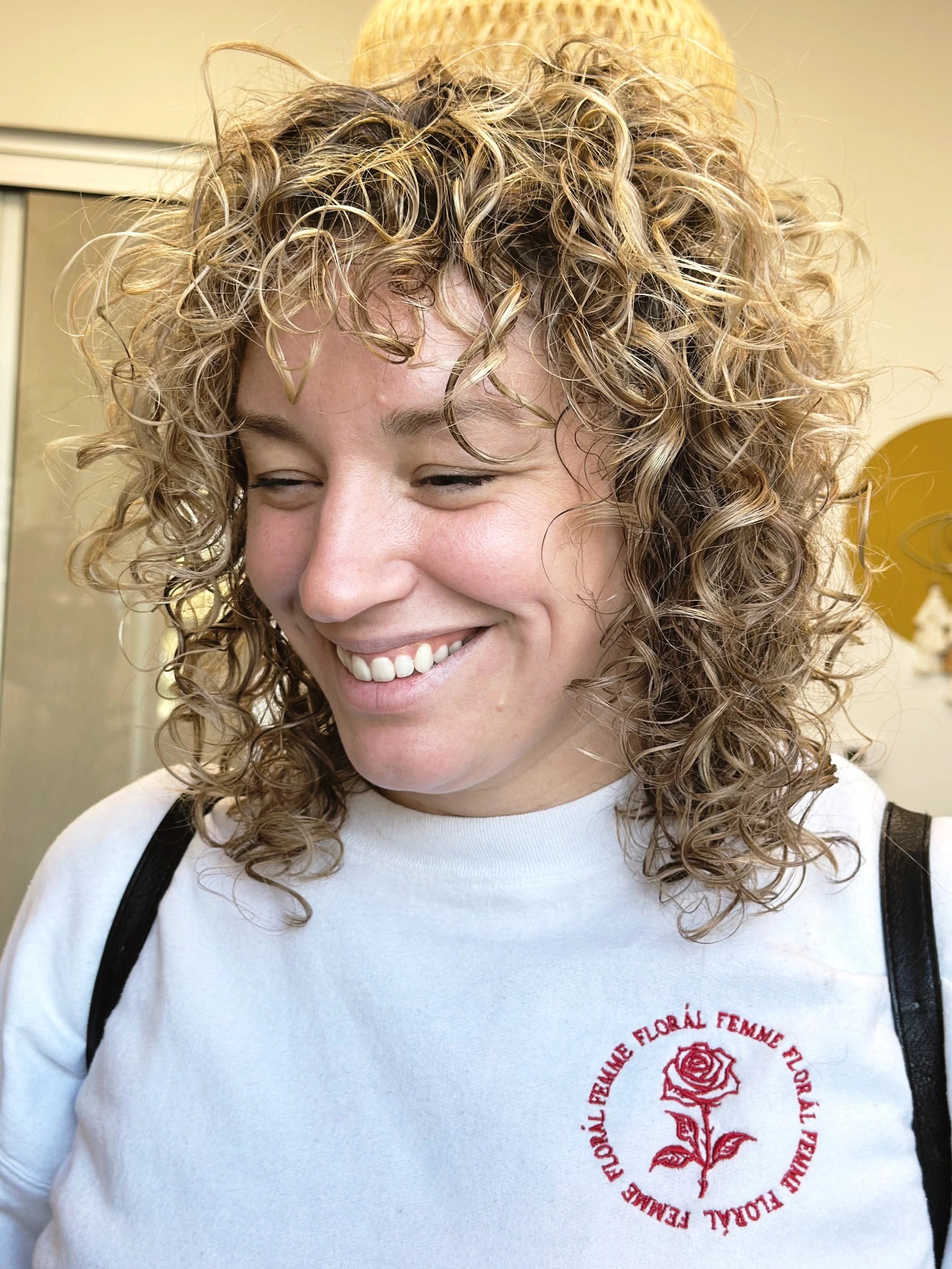 Photo of a client with shoulder-length blond curls with lots of volume and dimension.