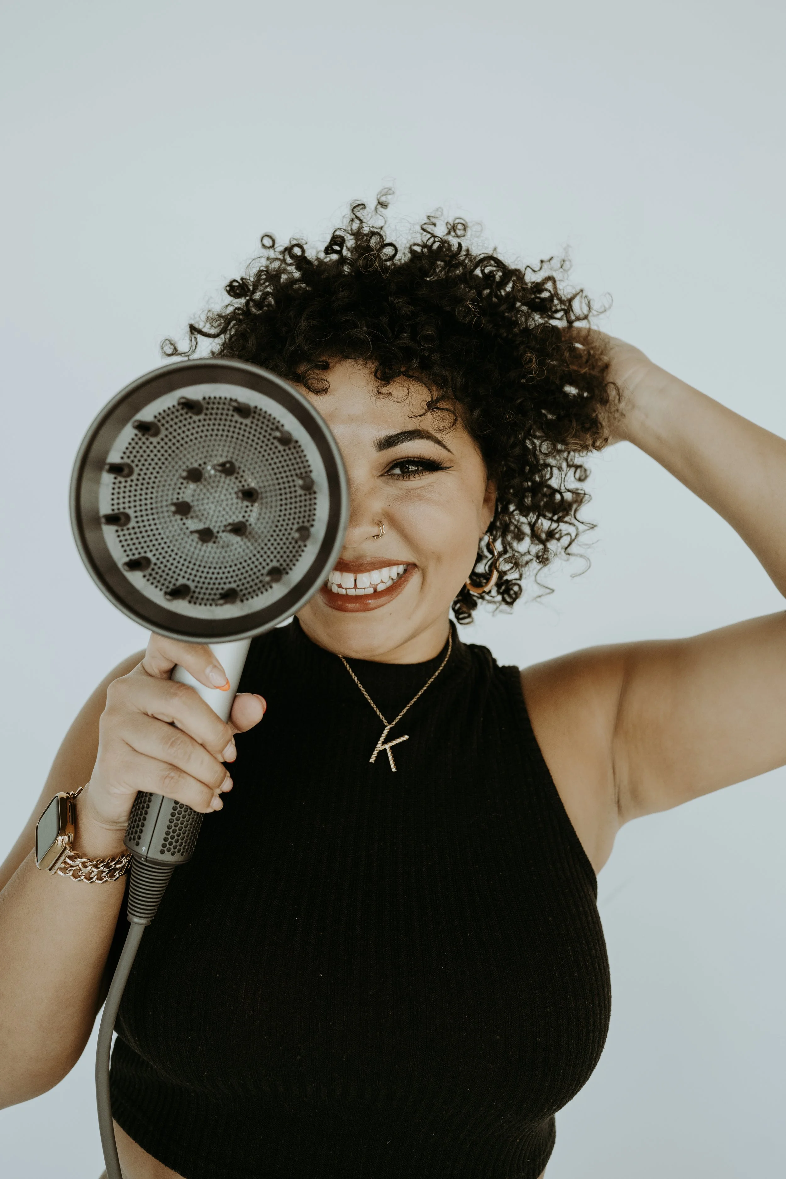 A phto of Ya Girl With the Curl, smiling at the camera while holding a diffuser up to her face.