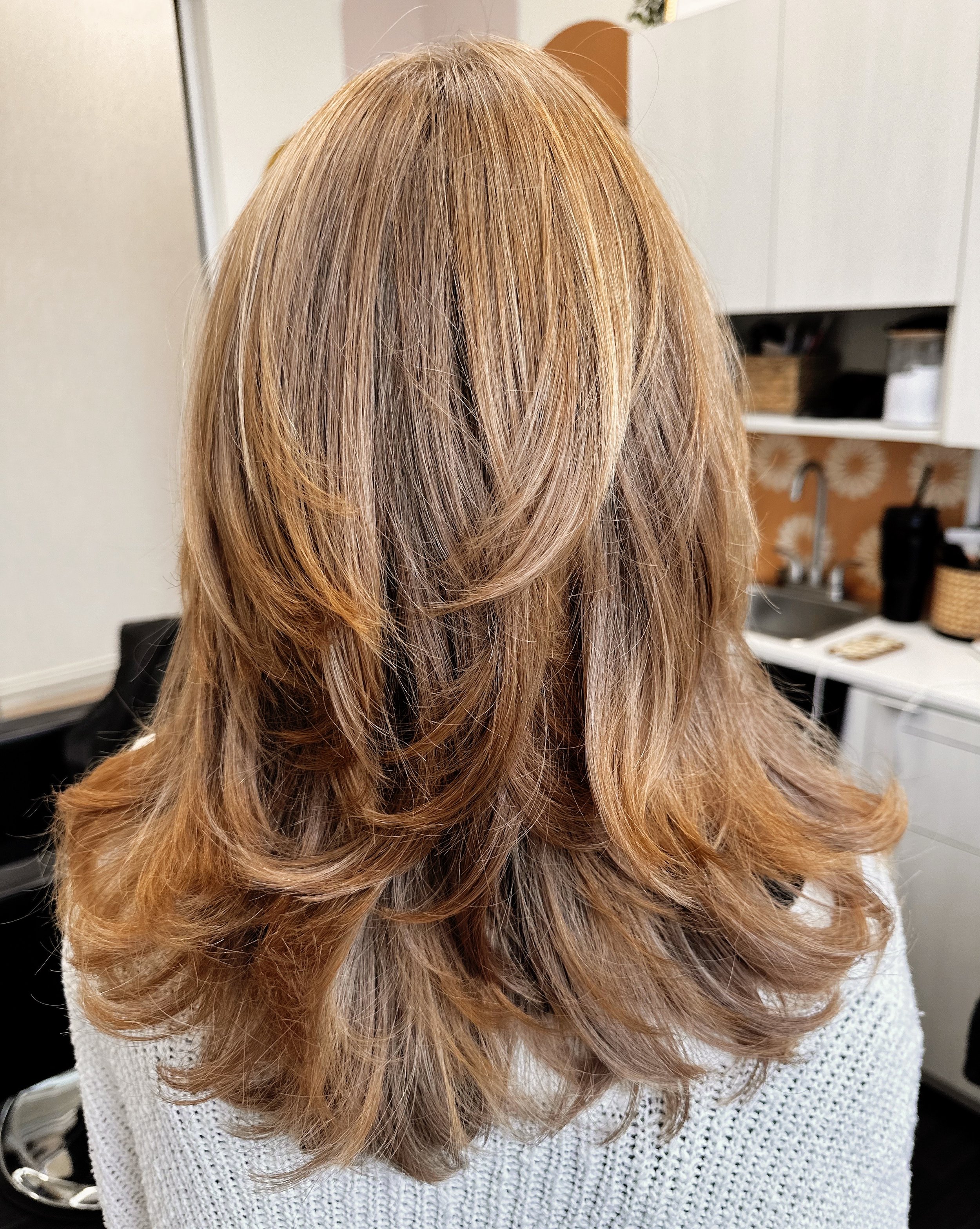 Photo of a client with long, honey-colored hair with lots of dimension, styled into soft waves. 