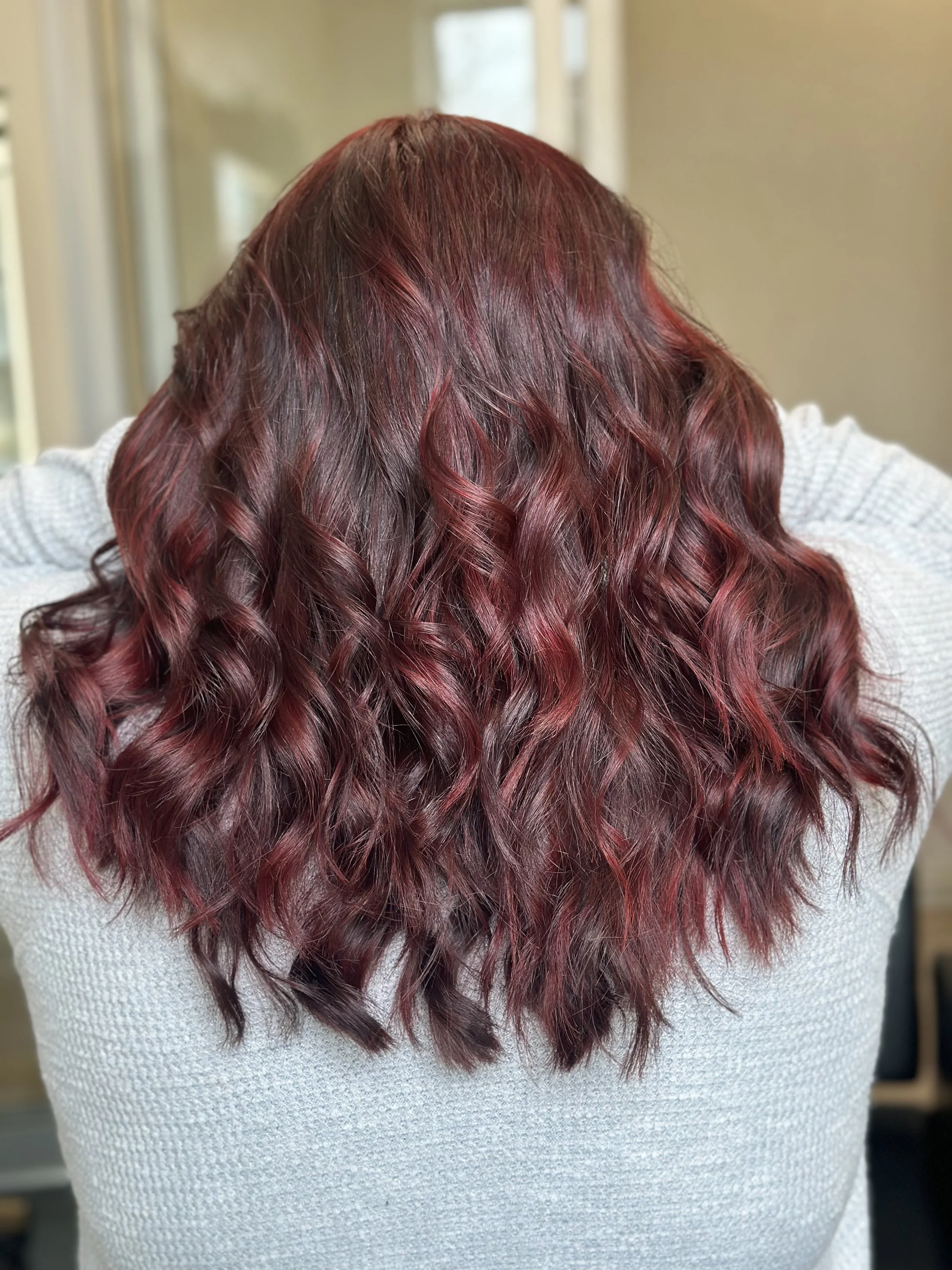 Photo of a client with long hair featuring vibrant red highlights and lots of dimension, styled in soft curls.