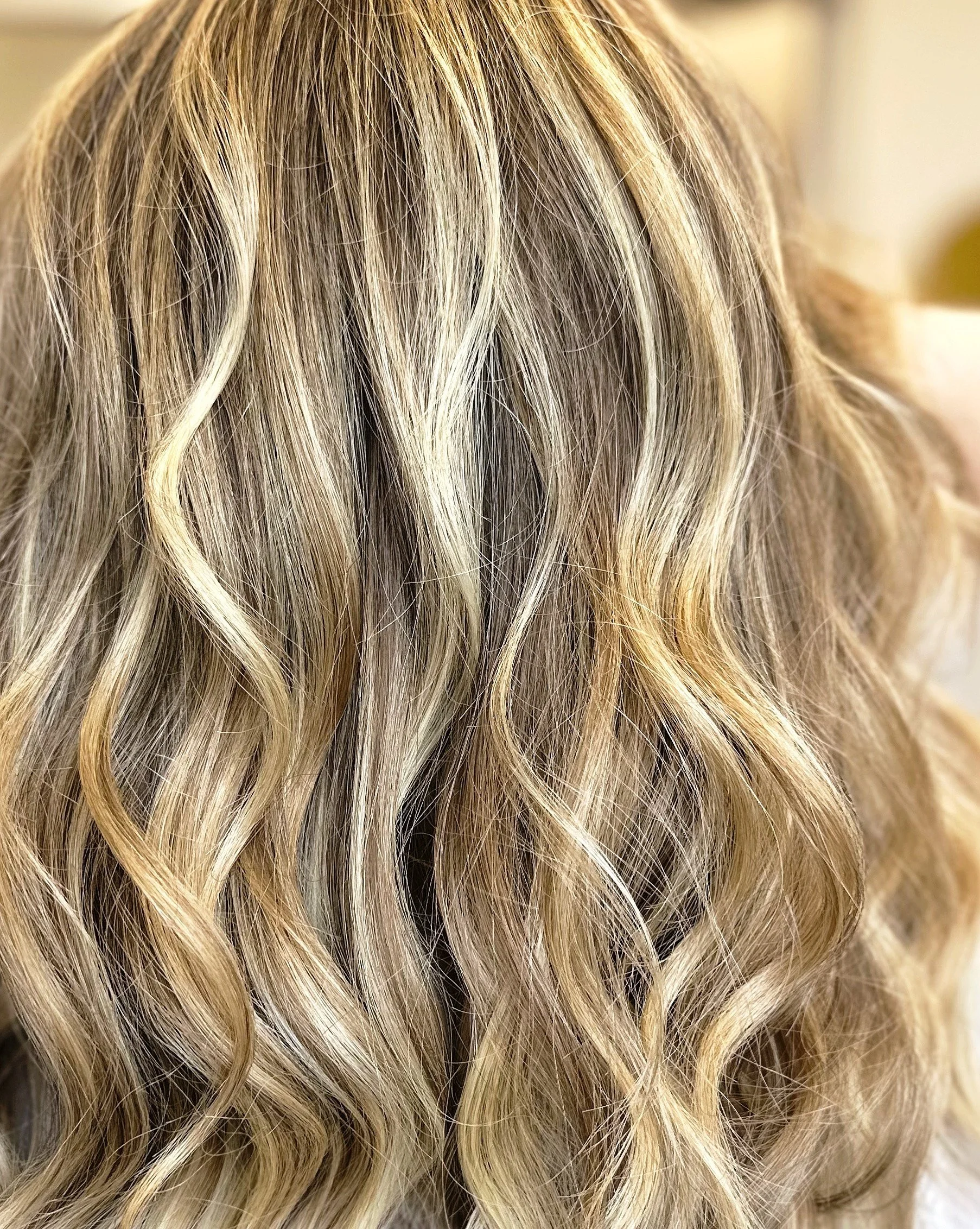 A close-up photo of healthy blond hair with lots of dimension and soft waves. 