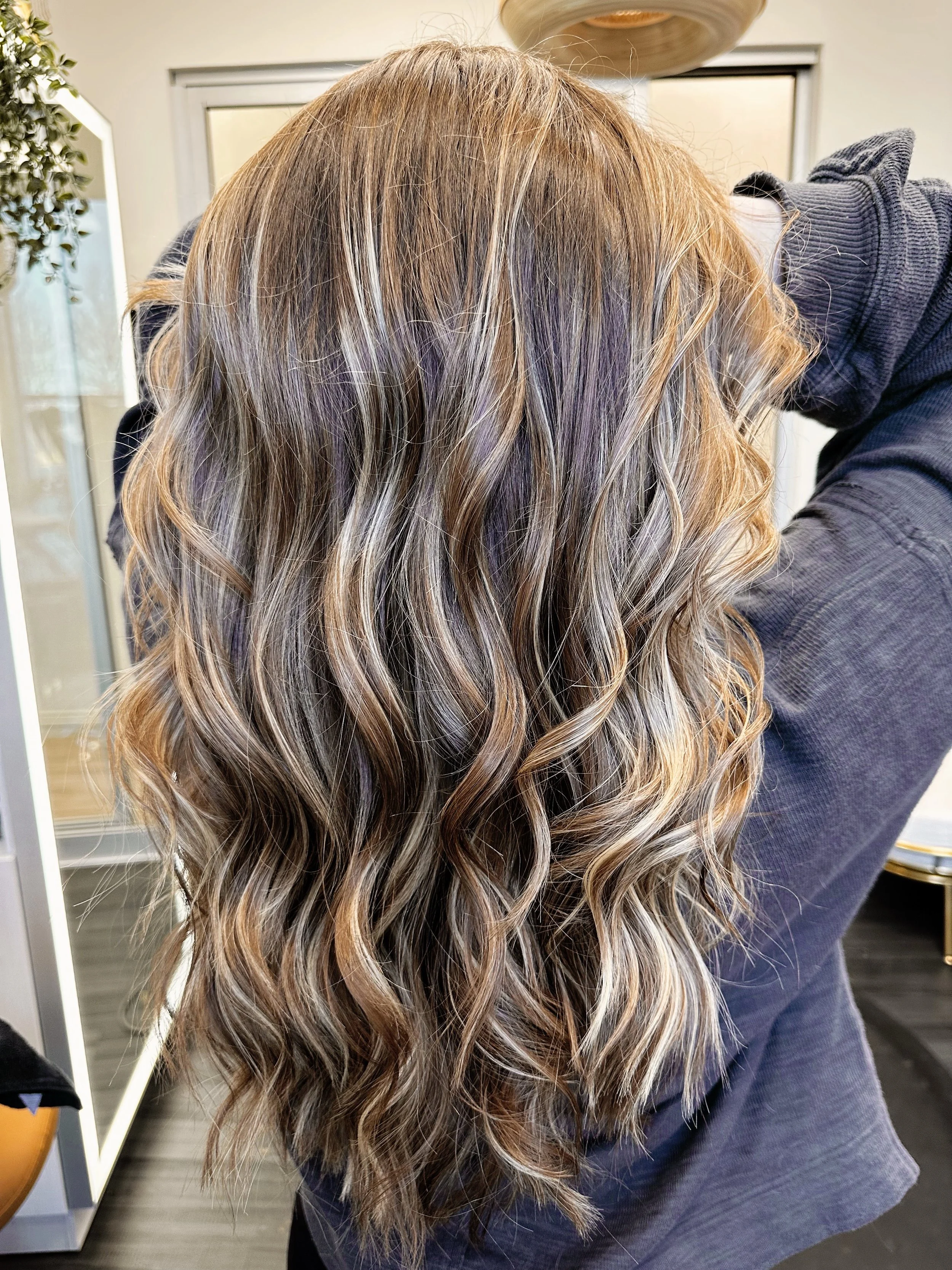 Photo of a client with long, wavy hair showcasing a healthy balayage service.