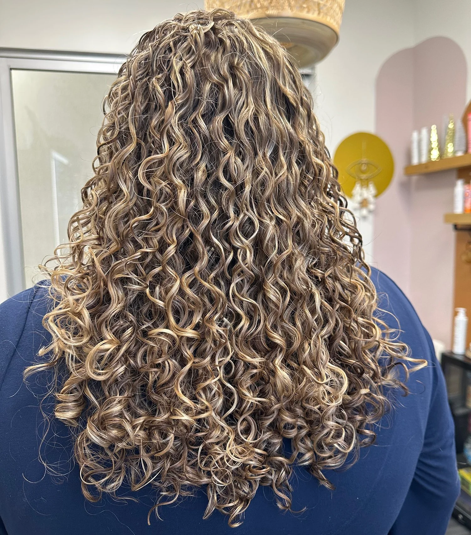 A photo of a client with long, curly hair with lots of brightness and dimension.
