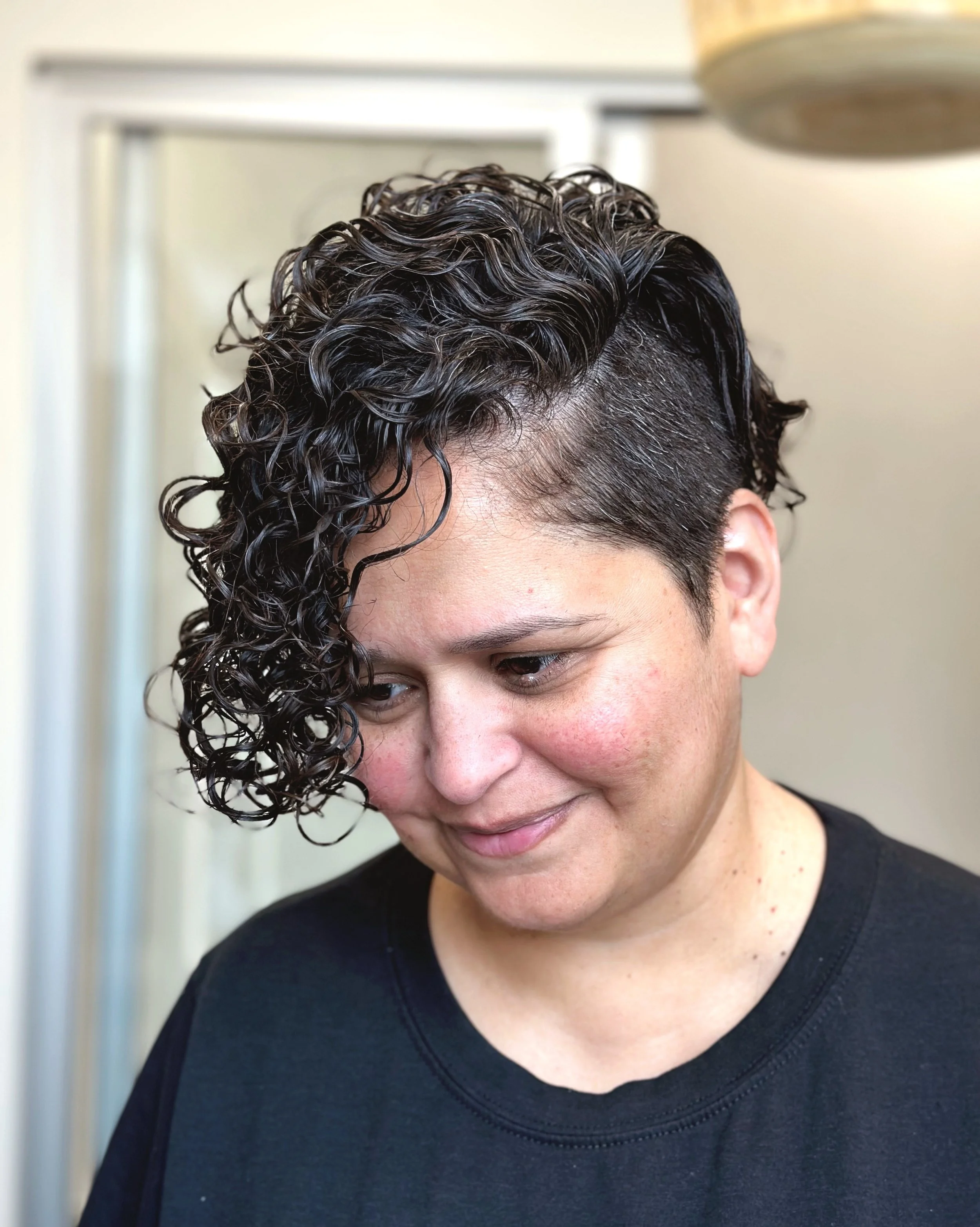 Photo of a client with curly chin-length dark hair and shaved (clipper cut) sides.
