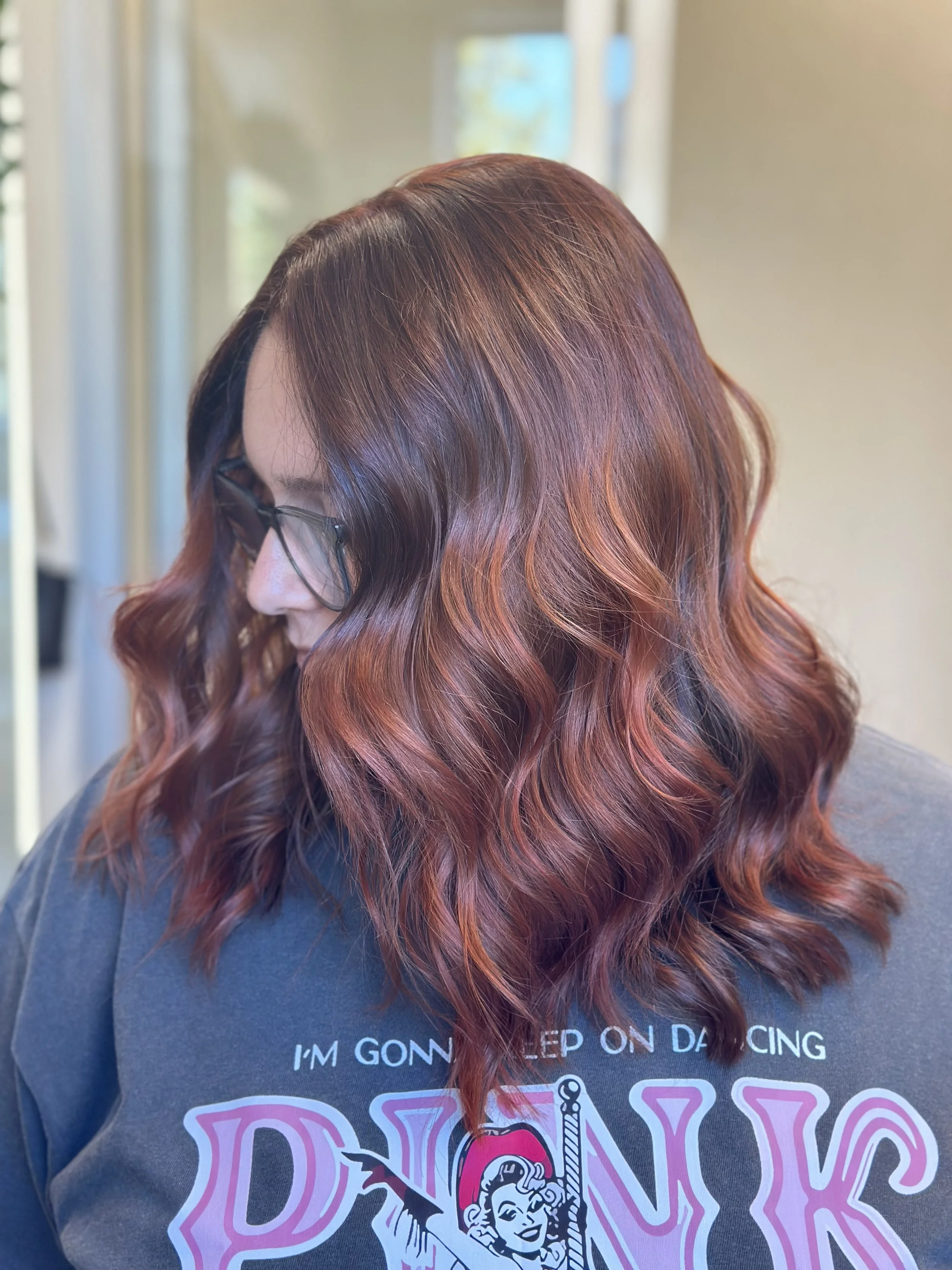 Photo of a client with long, thick, wavy hair with red highlights and lots of dimension.