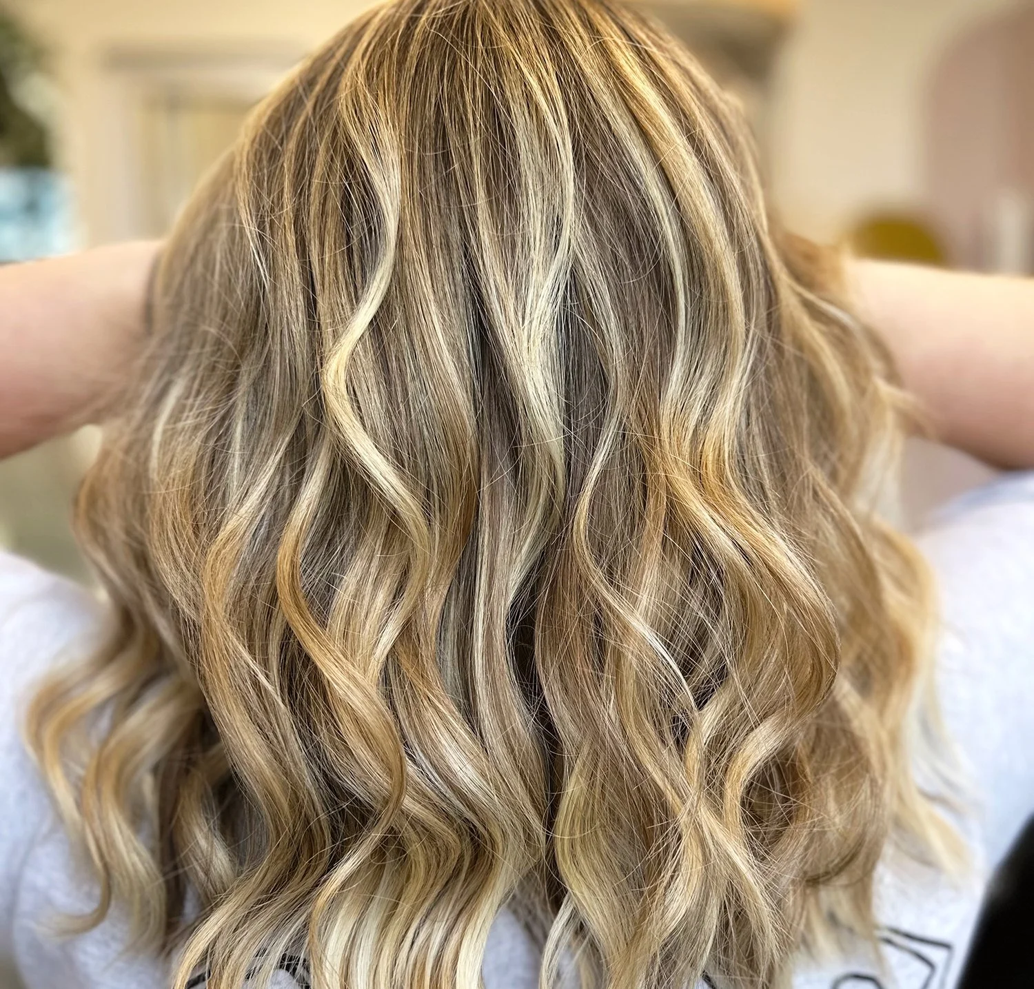 A close-up photo of the back of a client's head showing a blond balayage with a stylish wave.