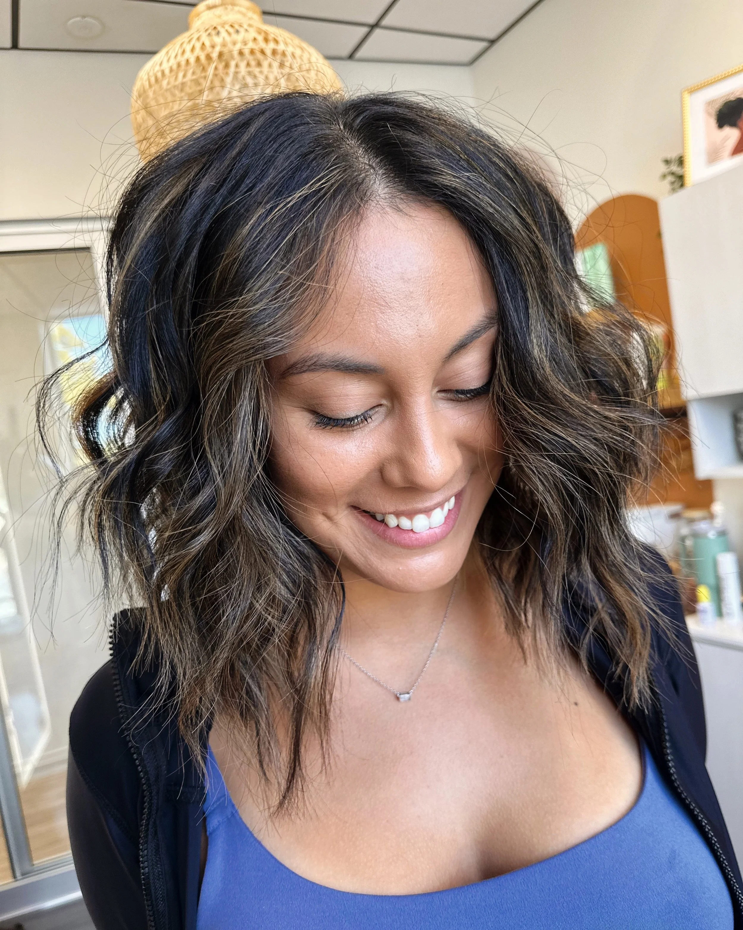 Photo of a client with dark brown shoulder-length hair featuring highlights, lots of dimension, and a soft wavy style.