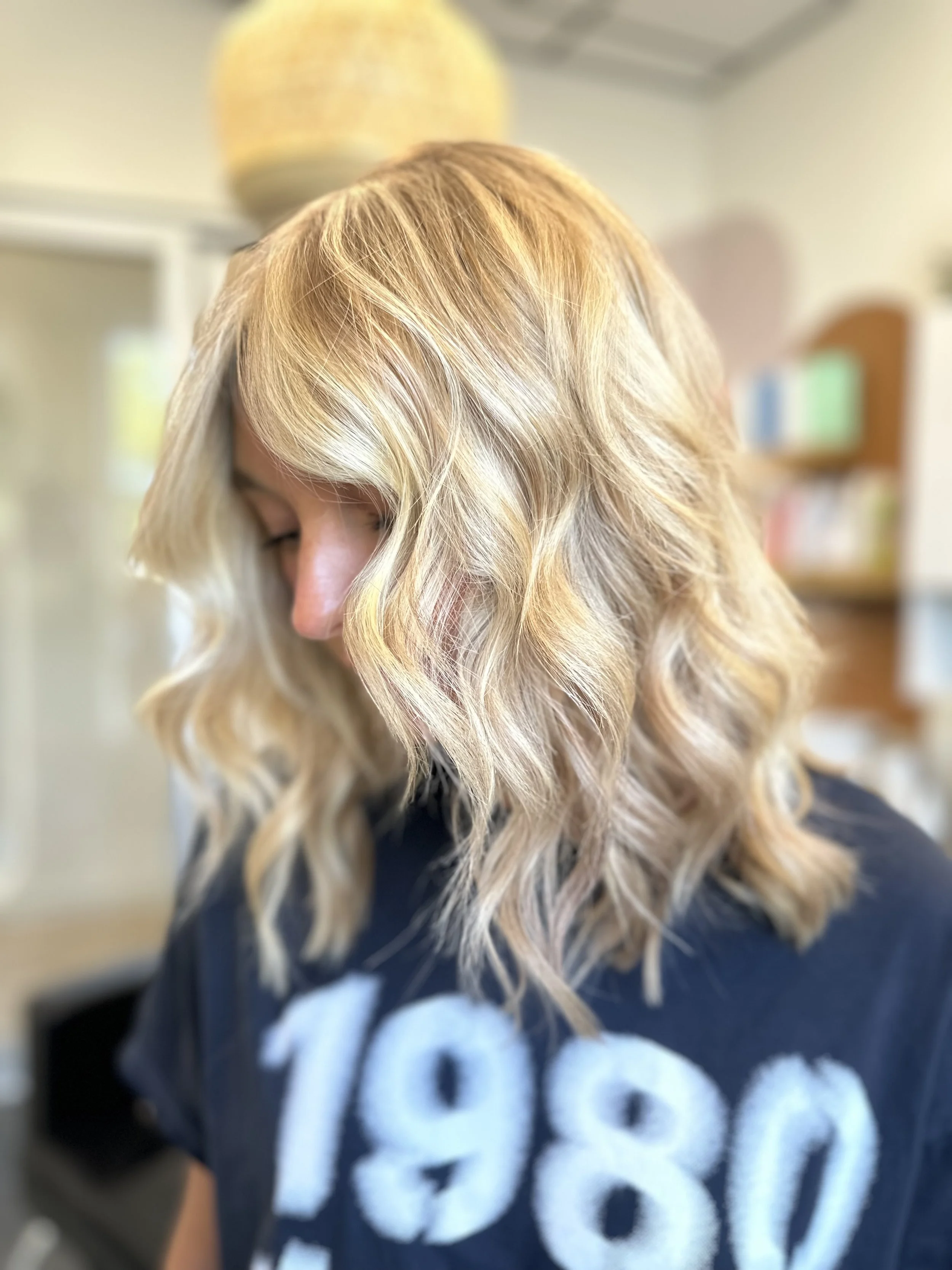Photo of a client with bright blond shoulder-length hair styled in soft beach waves.