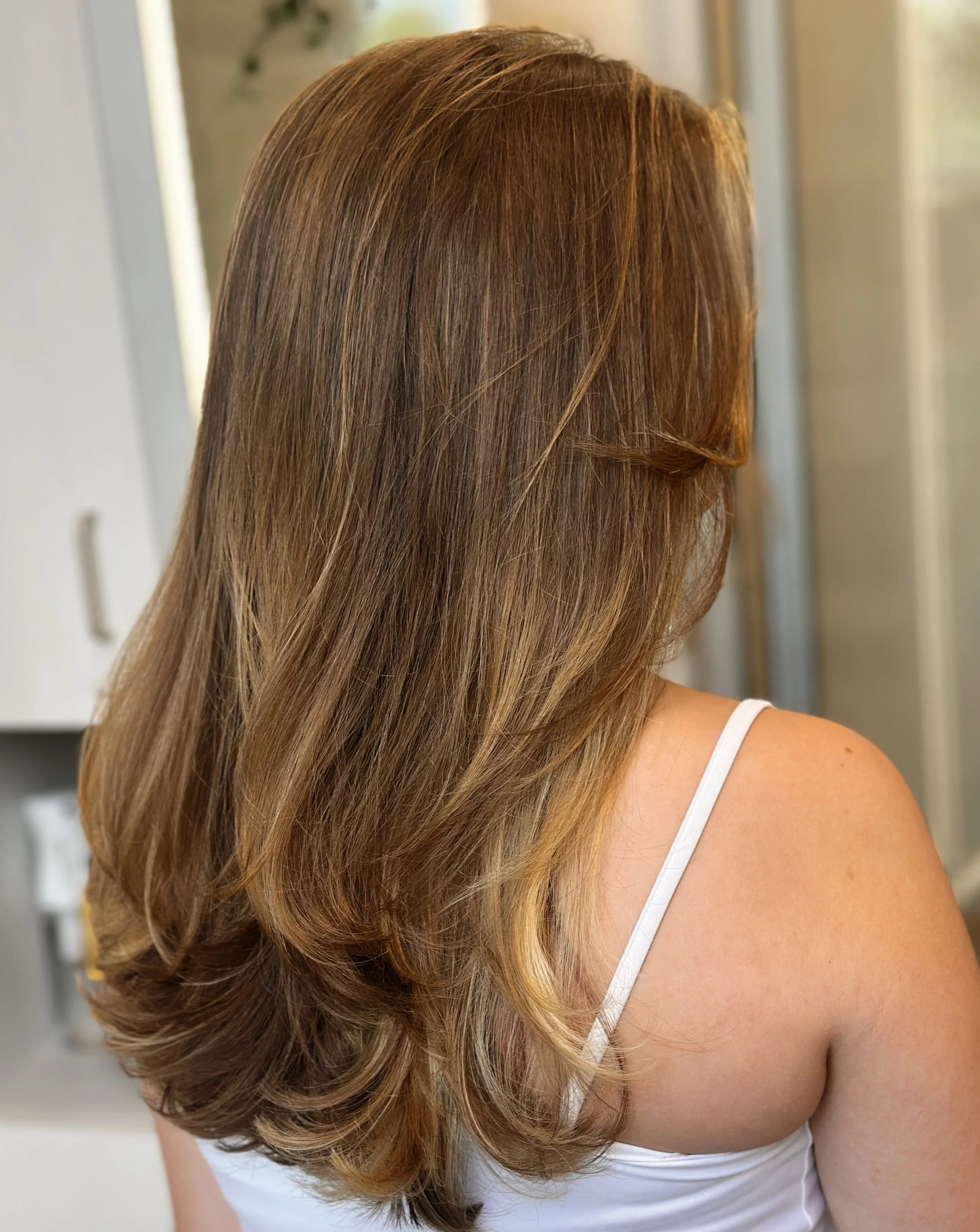 Photo of a client with long, honey-brown color, highlights, dimension, and soft wave styling.
