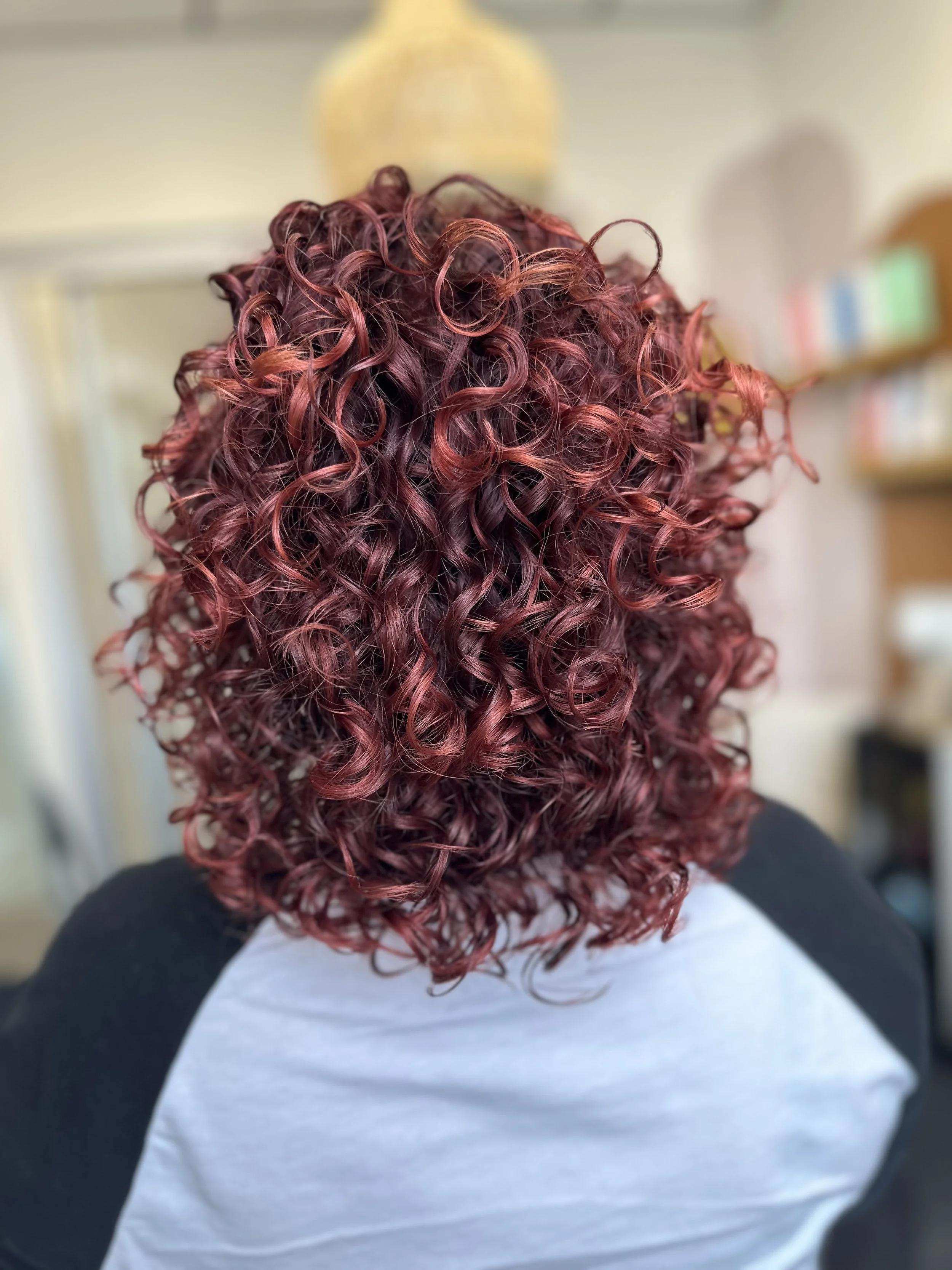 Photo of a client with lots of shoulder-length, voluminous curls in a dramatic red.