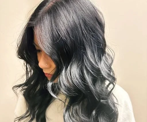 A photo of a client with dark wavy hair that looks super shiny and healthy after a root retouch.